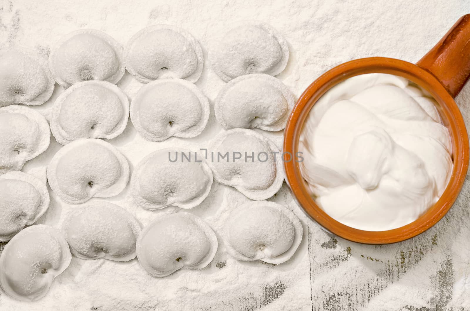 Dumplings and a Cup of sour cream, on boards, sprinkled with flour. by Gaina