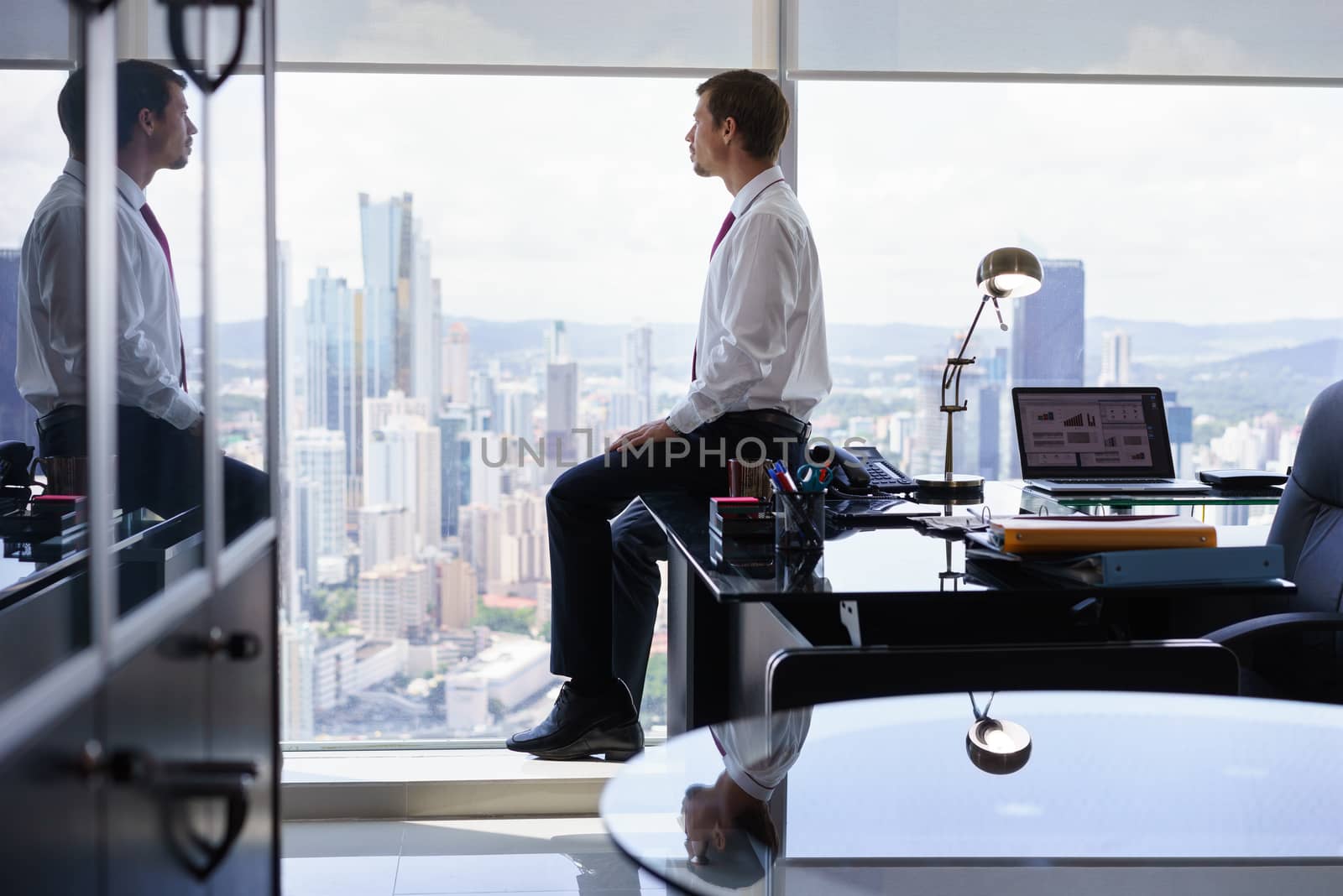 Business Person Sits On Desk Looking Out Of Office Window by diego_cervo