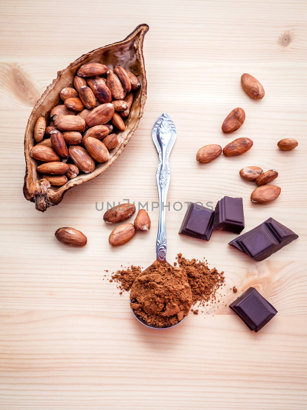 Brown chocolate powder in spoon , Roasted cocoa beans in the dry cocoa pod fruit and dark chocolate setup on wooden background.