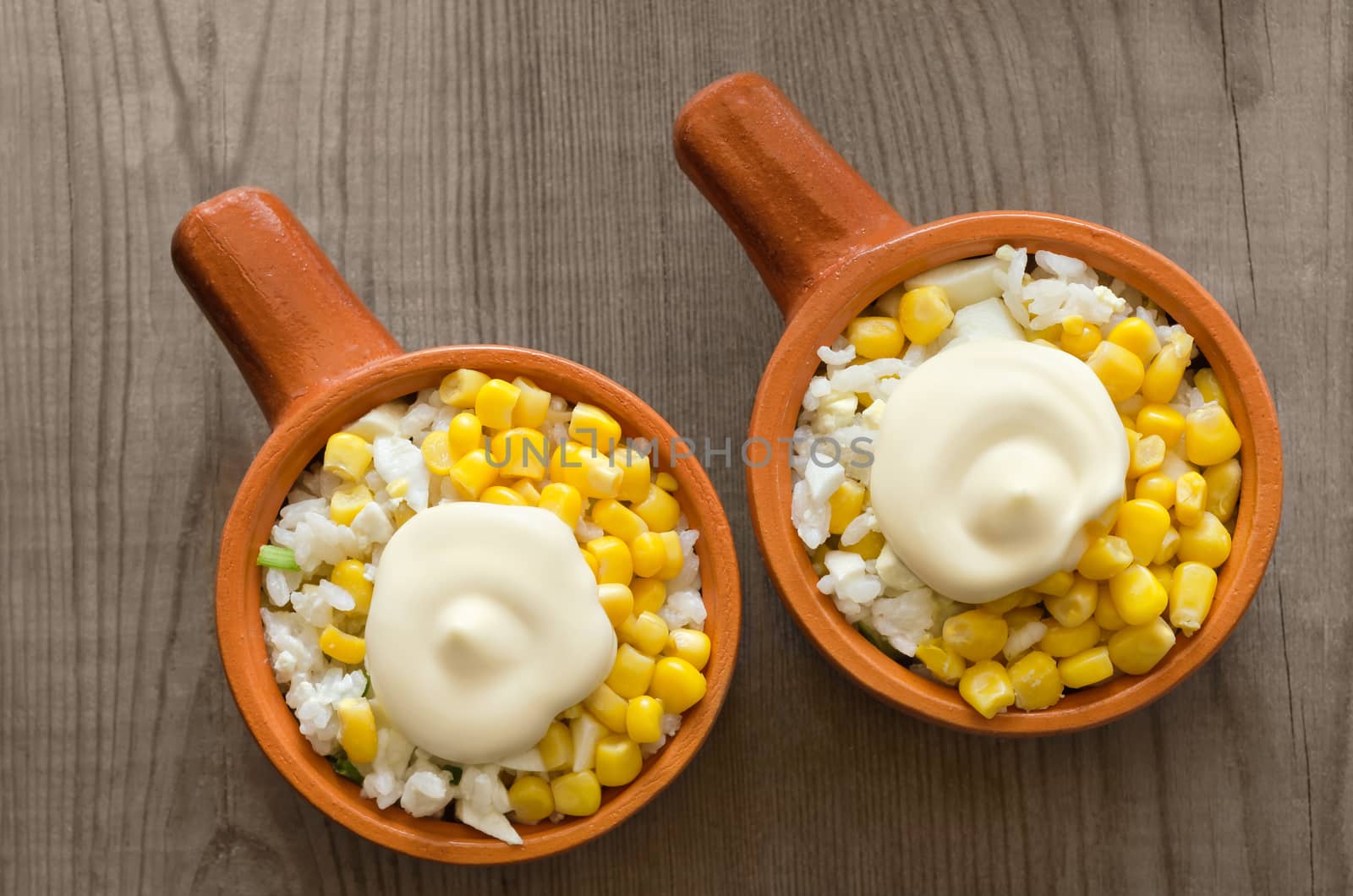 Rice salad and canned corn with mayonnaise, on a gray wooden background.