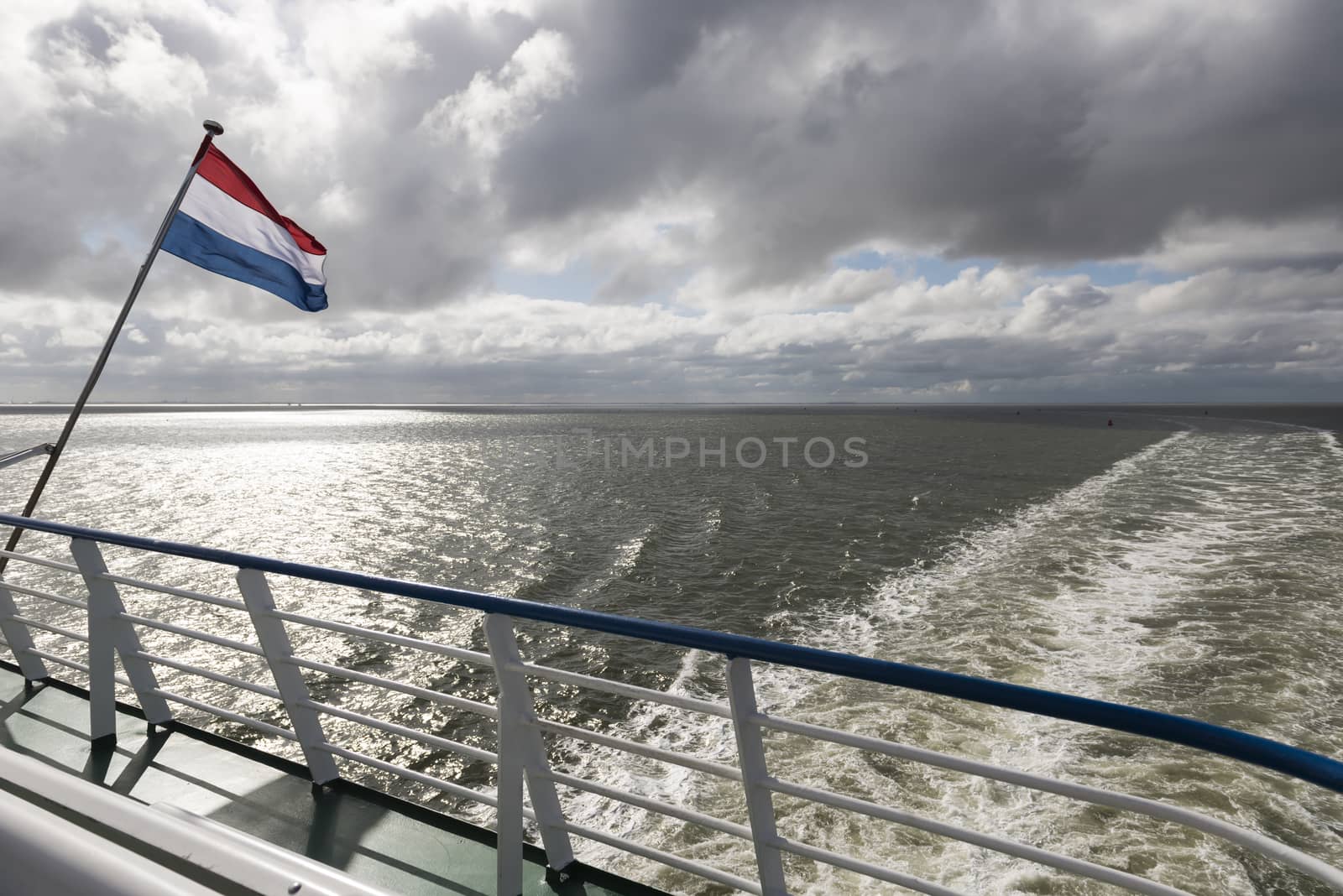 Wadden Sea with Dutch flag and wake as seen from the ferry

