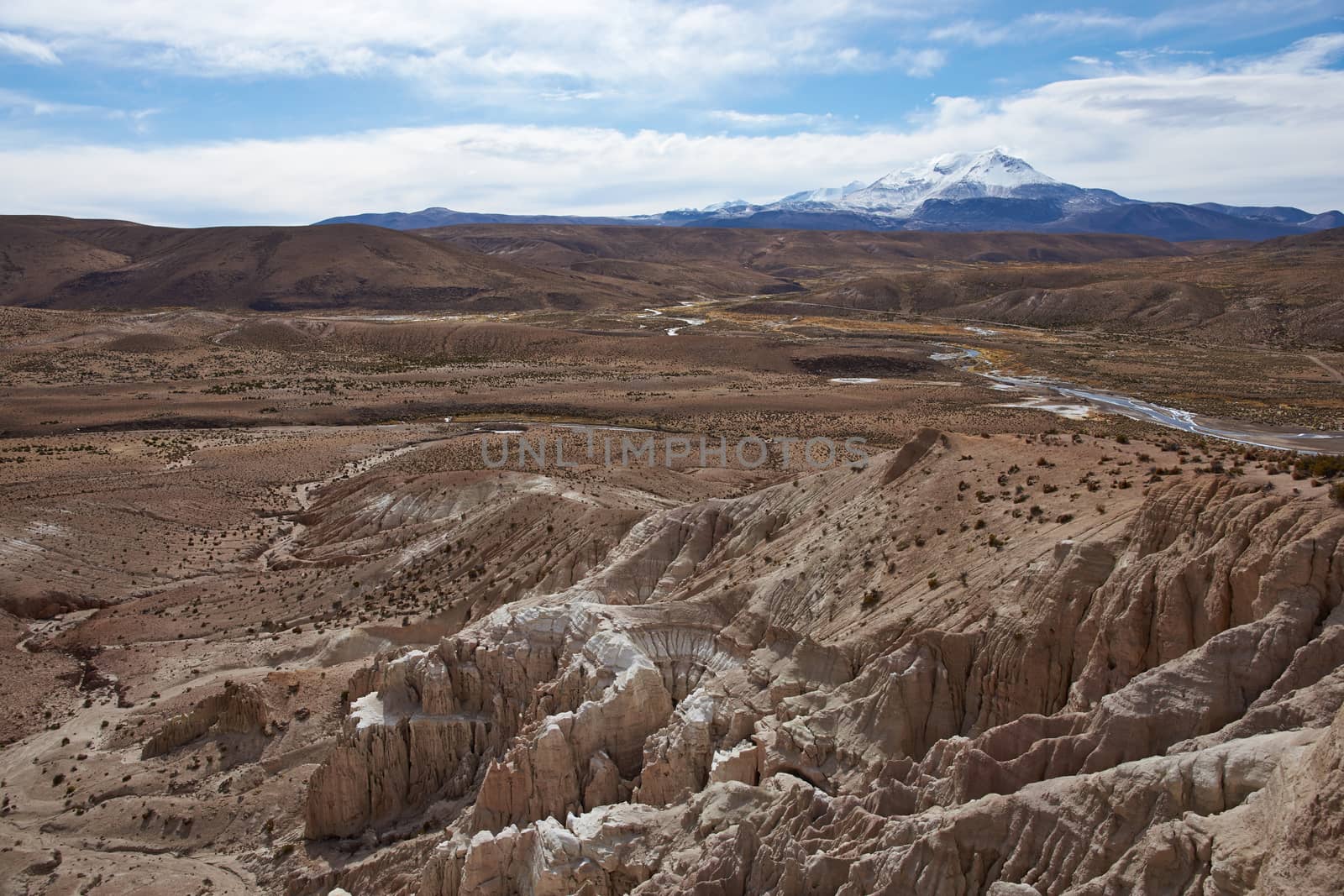 Eroded rock formations at the head of a river valley feeding the River Lauca high up on the Altiplano of northern Chile in Lauca National Park. In the background is the snow capped active Guallatiri volcano (6063 m).