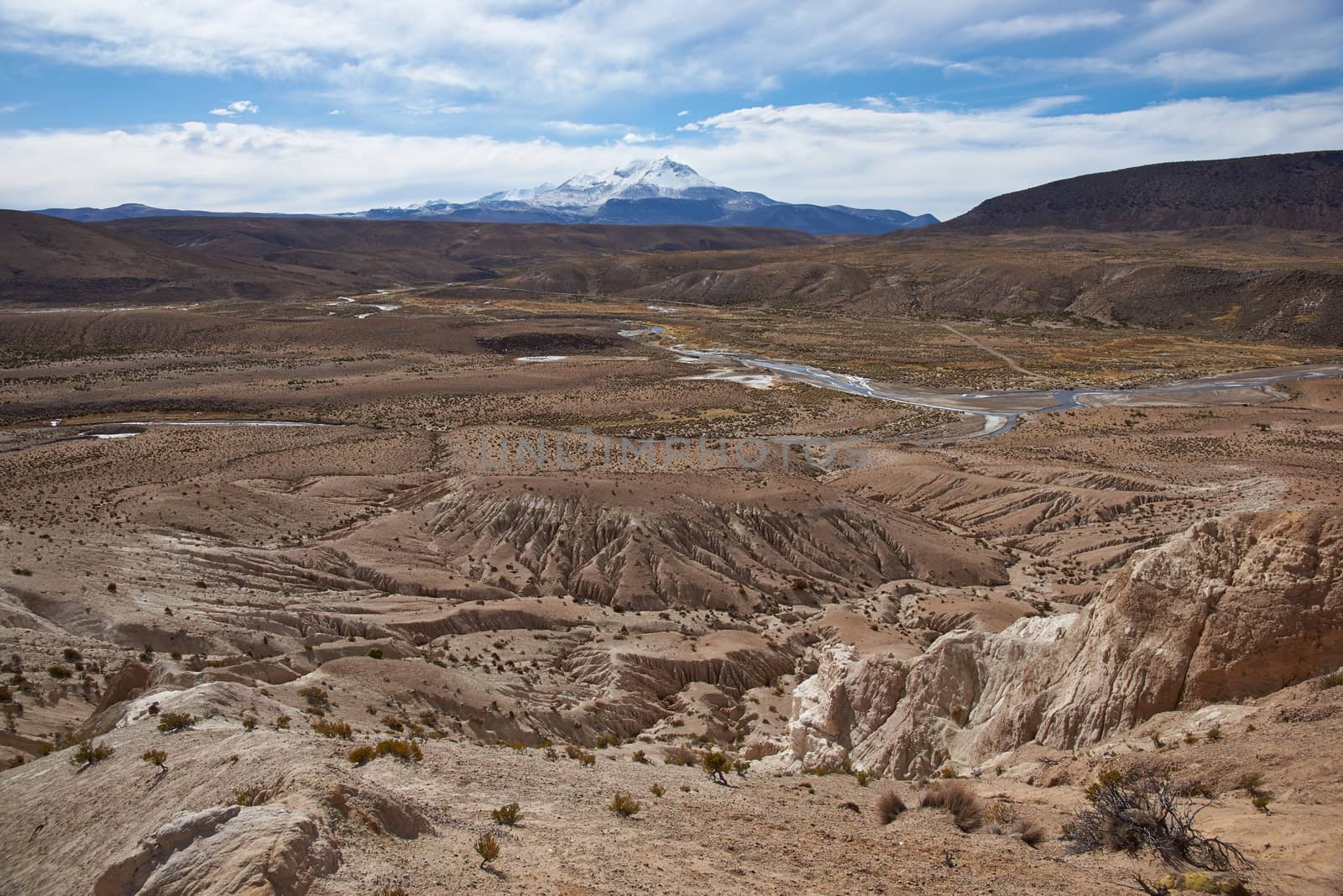 Eroded rock formations at the head of a river valley feeding the River Lauca high up on the Altiplano of northern Chile in Lauca National Park. In the background is the snow capped active Guallatiri volcano (6063 m).
