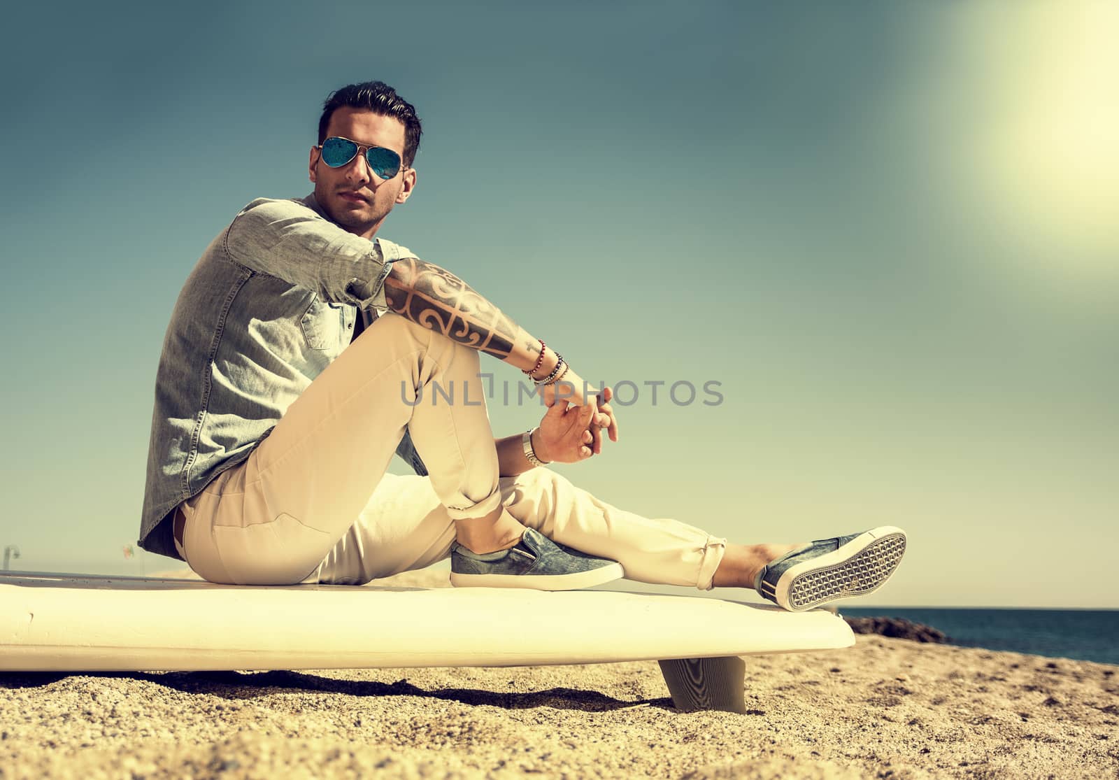 Handsome man sitting on surfboard at beach by artofphoto