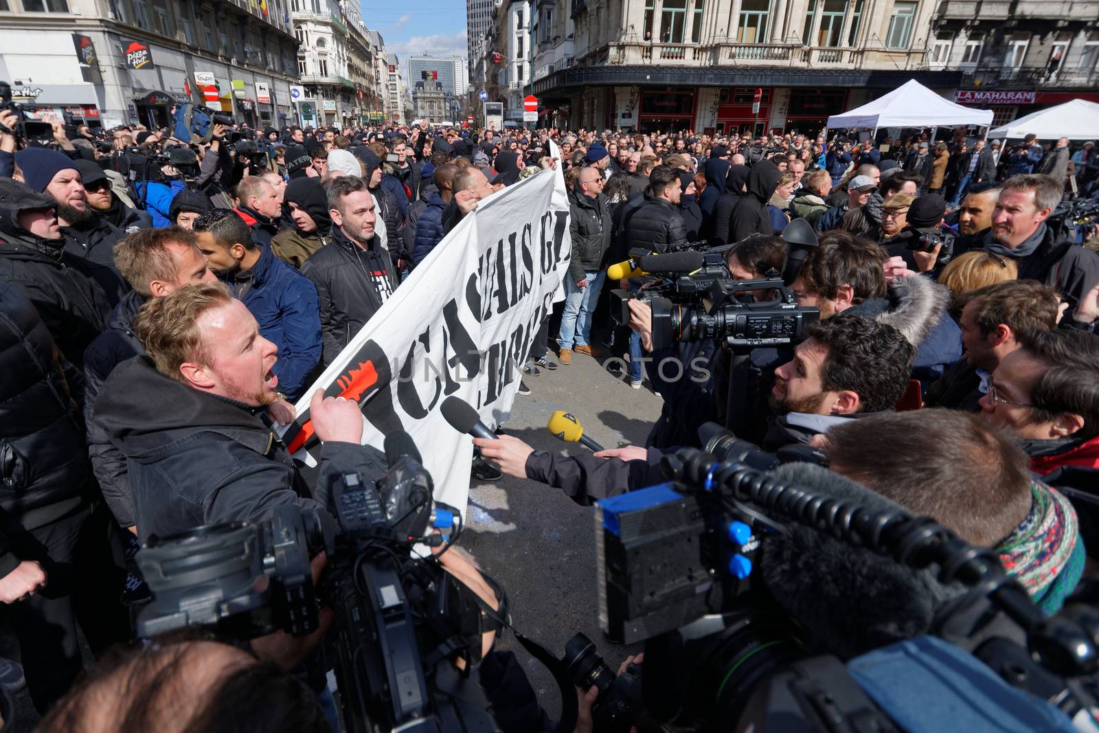 BELGIUM, Brussels : Far-right football hooligans chant slogans as they hold a banner of the FCK-Casuals hooligan movement, as they arrive in the square outside the stock exchange in Brussels on March 27, 2016 an area which has become an unofficial shrine to victims of the March 22, terror attacks claimed by the Islamic State (IS) group in which 31 people were killed and over 300 injured.Police fired water a cannon at far-right football hooligans who invaded a square in the Belgian capital that has become a memorial to the victims of the Brussels attacks, an AFP journalist said. Police took action after about 200 black-clad hooligans shouting nationalist and anti-immigrant slogans moved in on the Place de la Bourse where people were gathering in a show of solidarity with the victims.