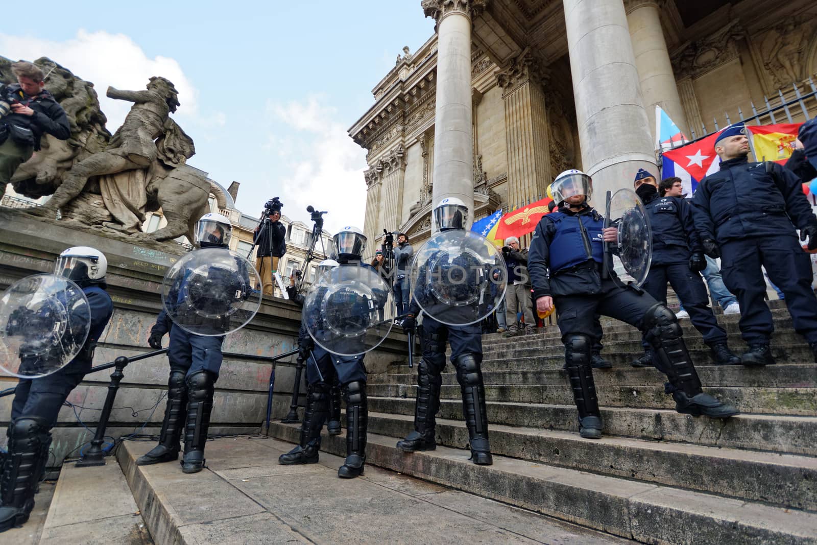 BELGIUM, Brussels : Belgian policemen stand guard as people gather at the makeshift memorial on the Place de la Bourse Square, in Brussels, on March 27, 2016 to pay tribute to the victims of the Brussels terror attacks which killed 31 people and injured over 300.Riot police fired water cannon on March 27, 2016 at far-right football hooligans who invaded a square in the Belgian capital that has become a memorial to the victims of the Brussels attacks, an AFP journalist said. Police took action after about 200 black-clad hooligans shouting nationalist and anti-immigrant slogans moved in on the Place de la Bourse where people were gathering in a show of solidarity with the victims. 