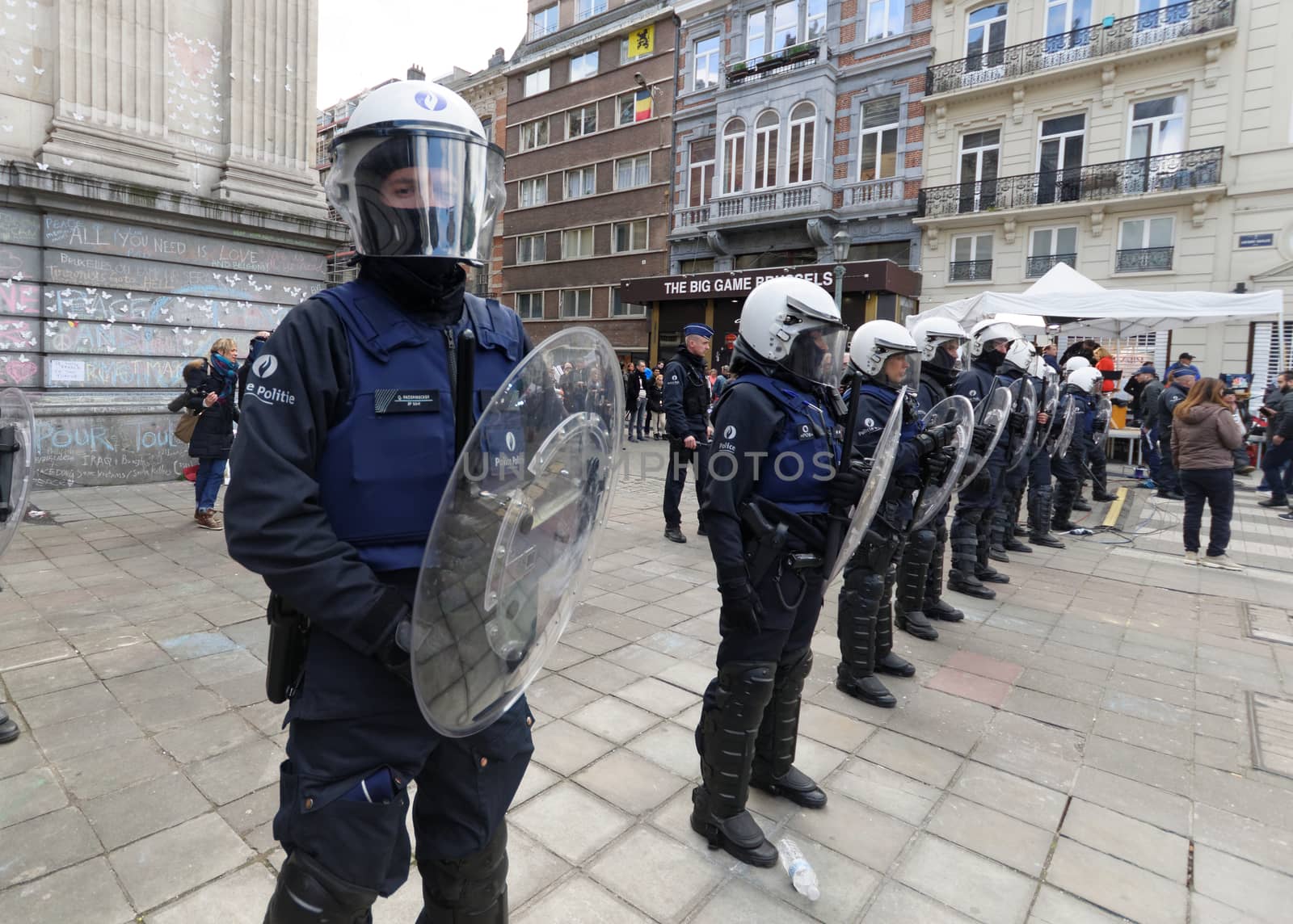 BELGIUM, Brussels : Belgian policemen stand guard as people gather at the makeshift memorial on the Place de la Bourse Square, in Brussels, on March 27, 2016 to pay tribute to the victims of the Brussels terror attacks which killed 31 people and injured over 300.Riot police fired water cannon on March 27, 2016 at far-right football hooligans who invaded a square in the Belgian capital that has become a memorial to the victims of the Brussels attacks, an AFP journalist said. Police took action after about 200 black-clad hooligans shouting nationalist and anti-immigrant slogans moved in on the Place de la Bourse where people were gathering in a show of solidarity with the victims. 