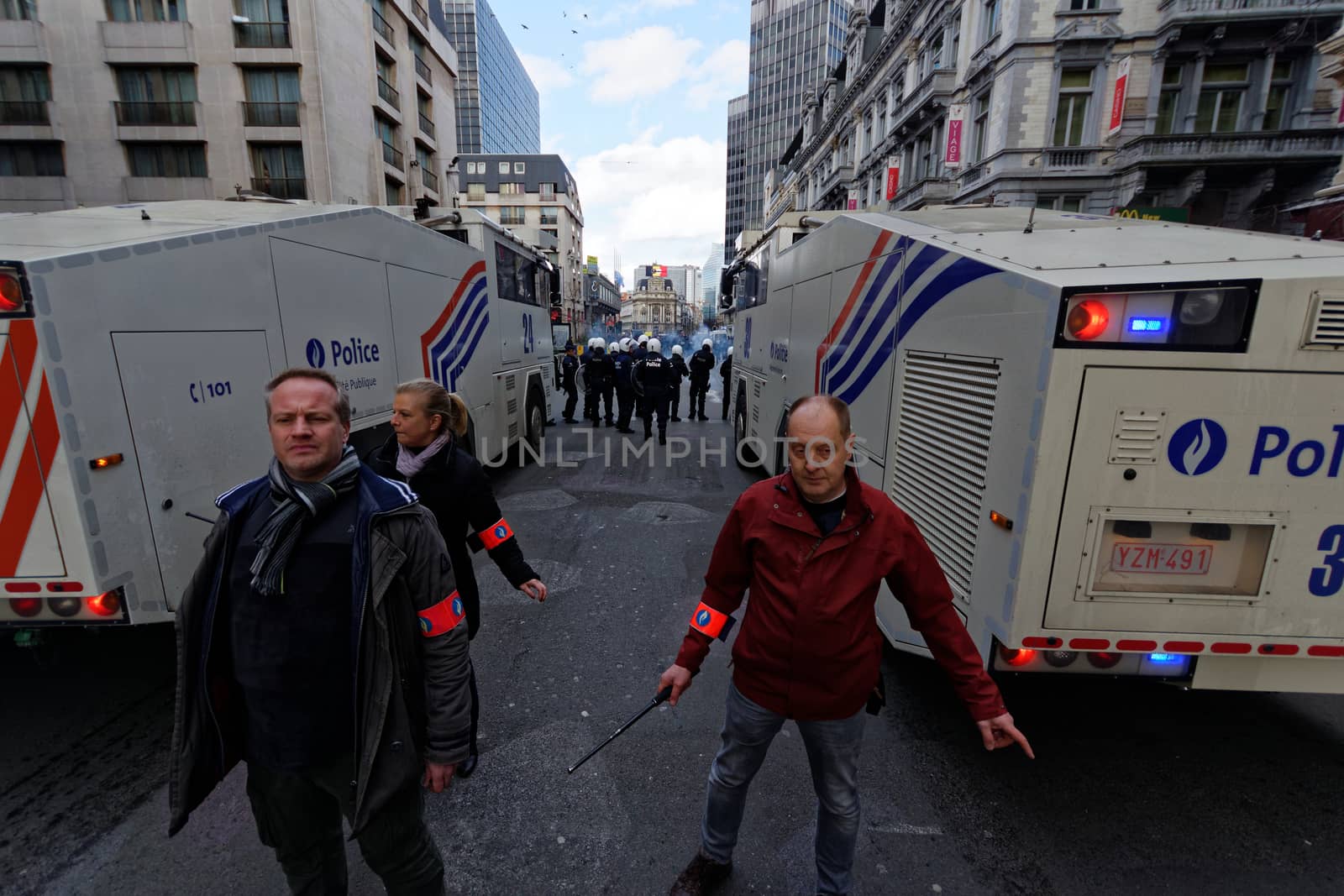 BELGIUM, Brussels : Belgian policemen stand guard as people gather at the makeshift memorial on the Place de la Bourse Square, in Brussels, on March 27, 2016 to pay tribute to the victims of the Brussels terror attacks which killed 31 people and injured over 300.Riot police fired water cannon on March 27, 2016 at far-right football hooligans who invaded a square in the Belgian capital that has become a memorial to the victims of the Brussels attacks, an AFP journalist said. Police took action after about 200 black-clad hooligans shouting nationalist and anti-immigrant slogans moved in on the Place de la Bourse where people were gathering in a show of solidarity with the victims. 