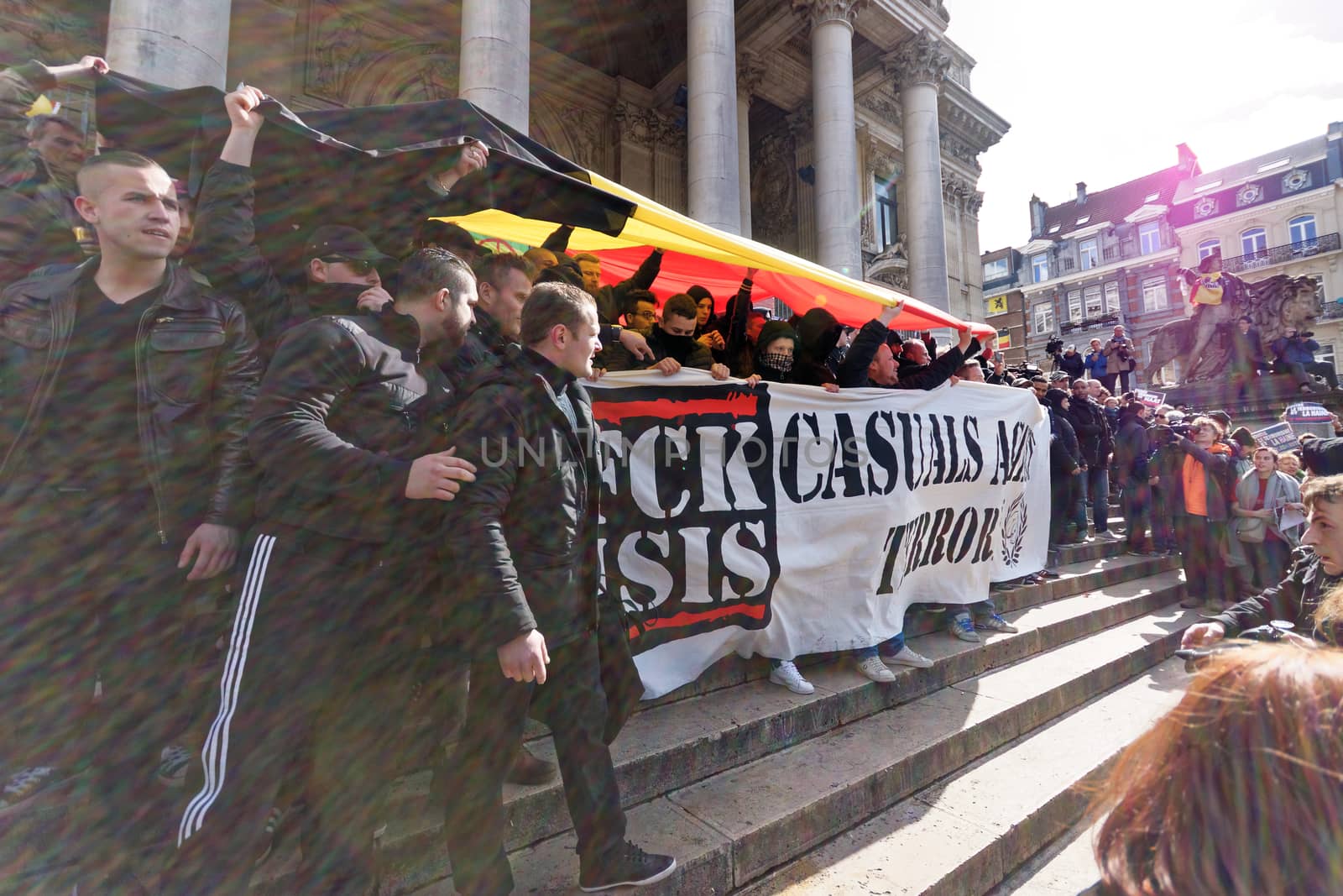 BELGIUM, Brussels : Far-right football hooligans chant slogans as they hold a banner of the FCK-Casuals hooligan movement, as they arrive in the square outside the stock exchange in Brussels on March 27, 2016 an area which has become an unofficial shrine to victims of the March 22, terror attacks claimed by the Islamic State (IS) group in which 31 people were killed and over 300 injured.Police fired water a cannon at far-right football hooligans who invaded a square in the Belgian capital that has become a memorial to the victims of the Brussels attacks, an AFP journalist said. Police took action after about 200 black-clad hooligans shouting nationalist and anti-immigrant slogans moved in on the Place de la Bourse where people were gathering in a show of solidarity with the victims.