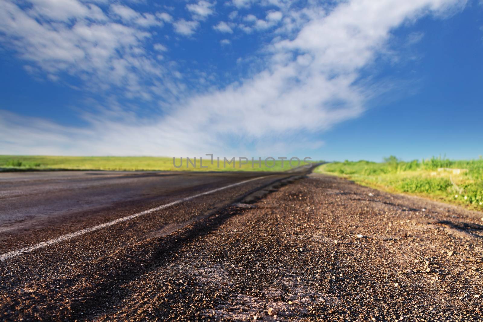 asphalt road through the green field and clouds on blue sky in summer day