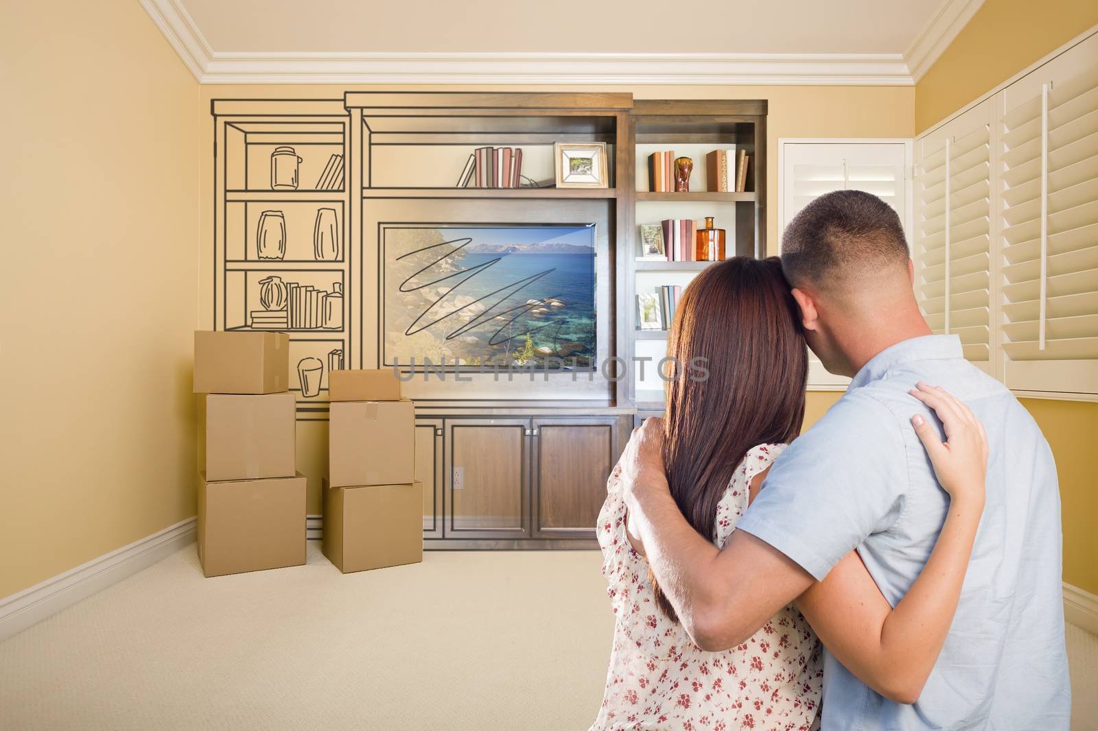 Young Military Couple Looking At Drawing of Entertainment Unit In Room With Moving Boxes.