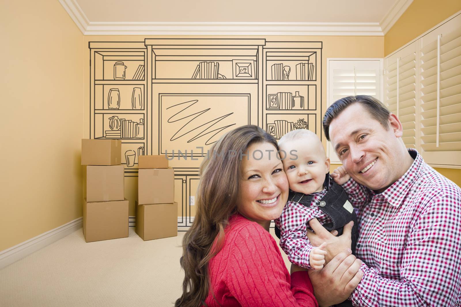 Young Family In Room With Moving Boxes and Drawing of Entertainment Unit On Wall.