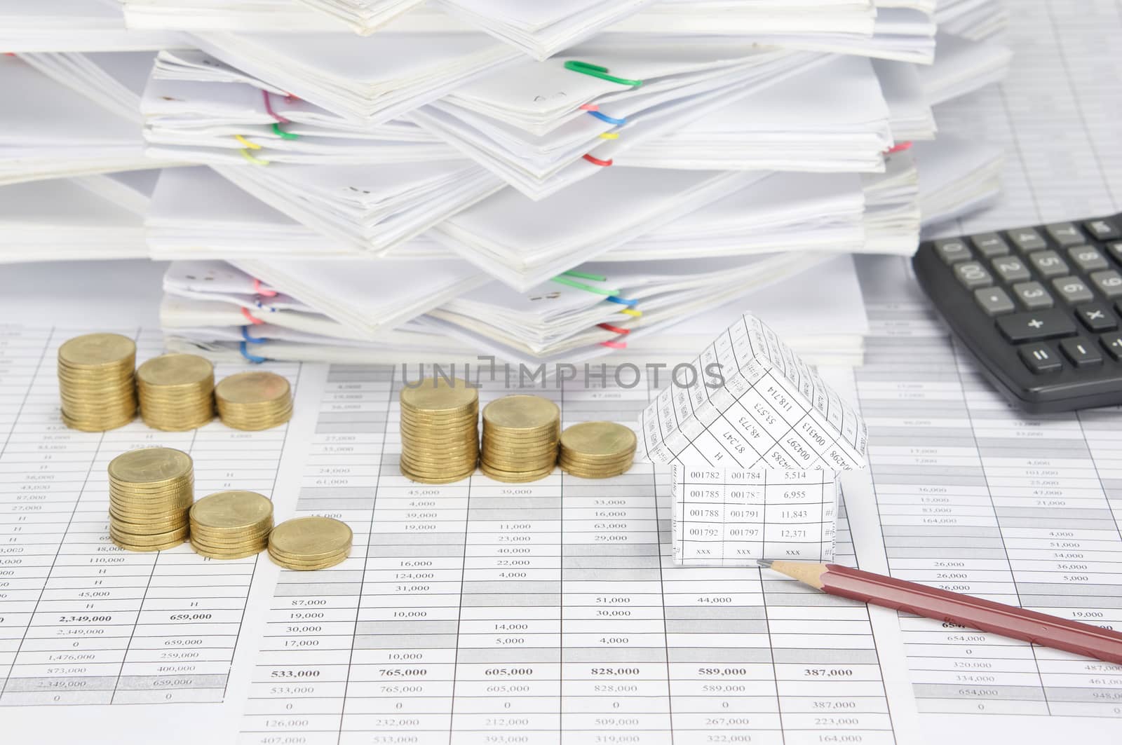 Brown pencil and house with step pile of gold coins on finance account have calculator and overload of paperwork with colorful paperclip as background.