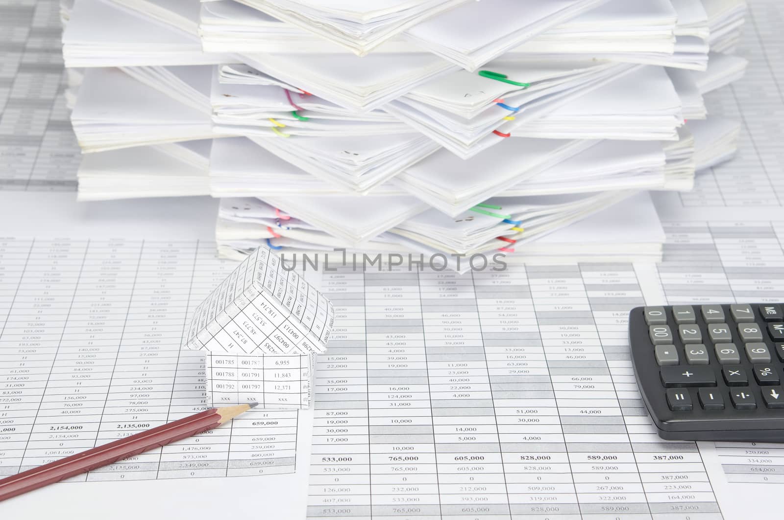 House and brown pencil on finance account have calculator and overload of paperwork with colorful paperclip as background.