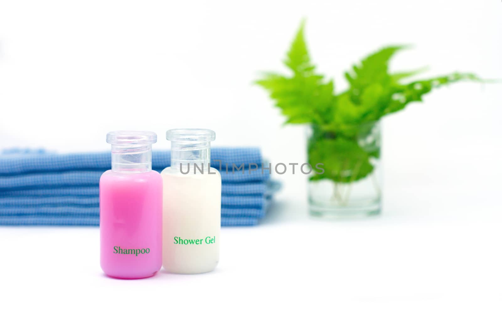 Shampoo and Shower gel on white background. Shampoo, Shower gel with blurred blue cloth and green leaves in a glass of water.