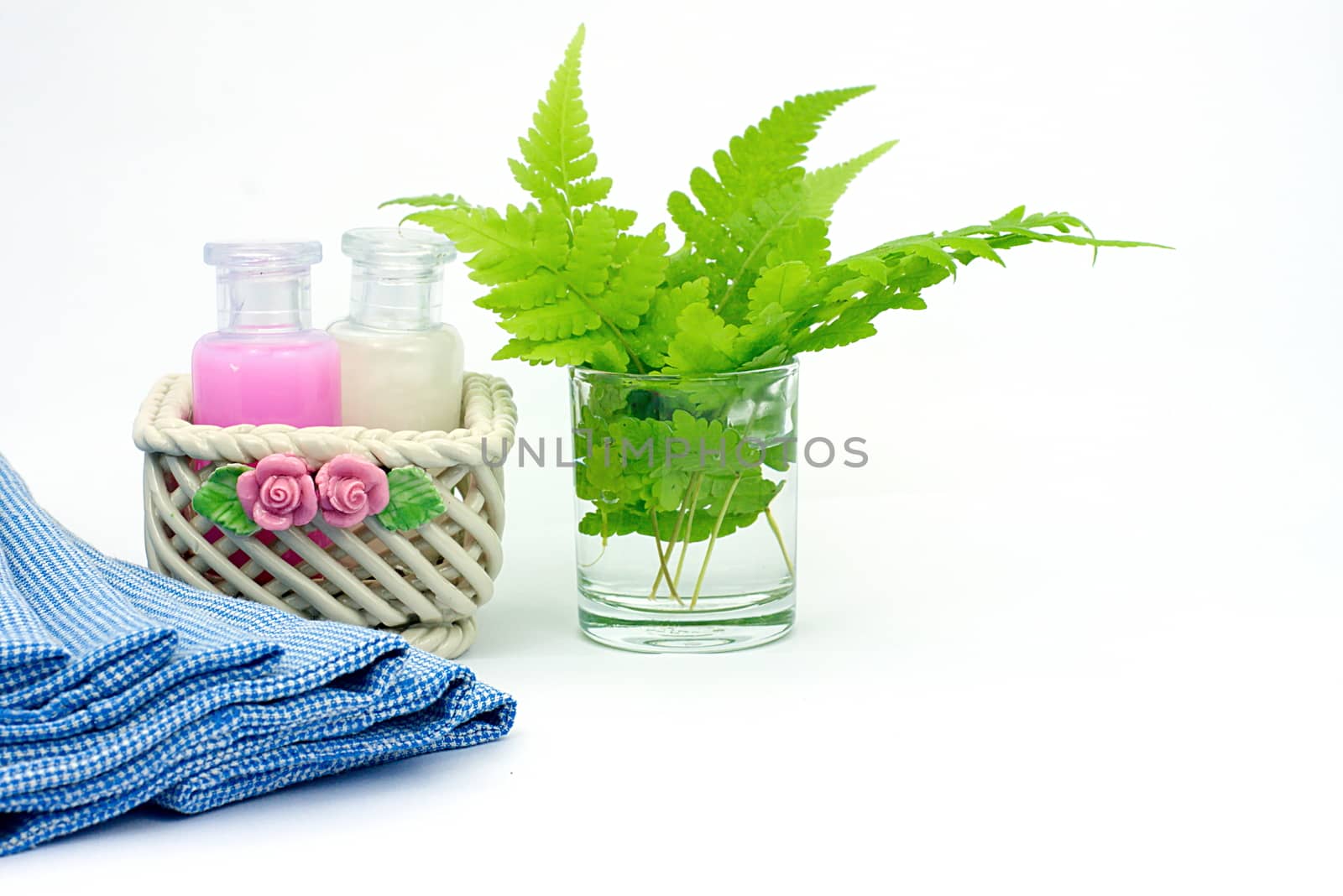 Shampoo and Shower gel put in ceramic basket on white background. Shampoo, Shower gel bottles with blue cloth and green leaves in a glass of water.