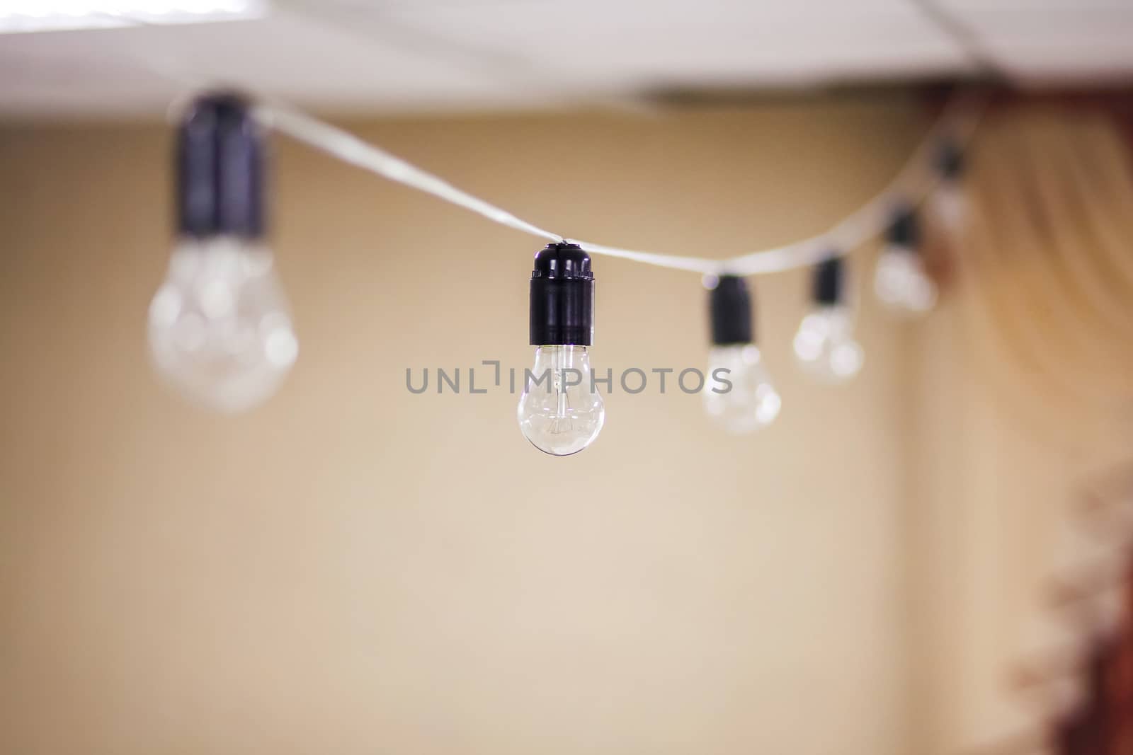 Electric bulb garland hanging indoor, turned off, shallow depth focus at central lamp.