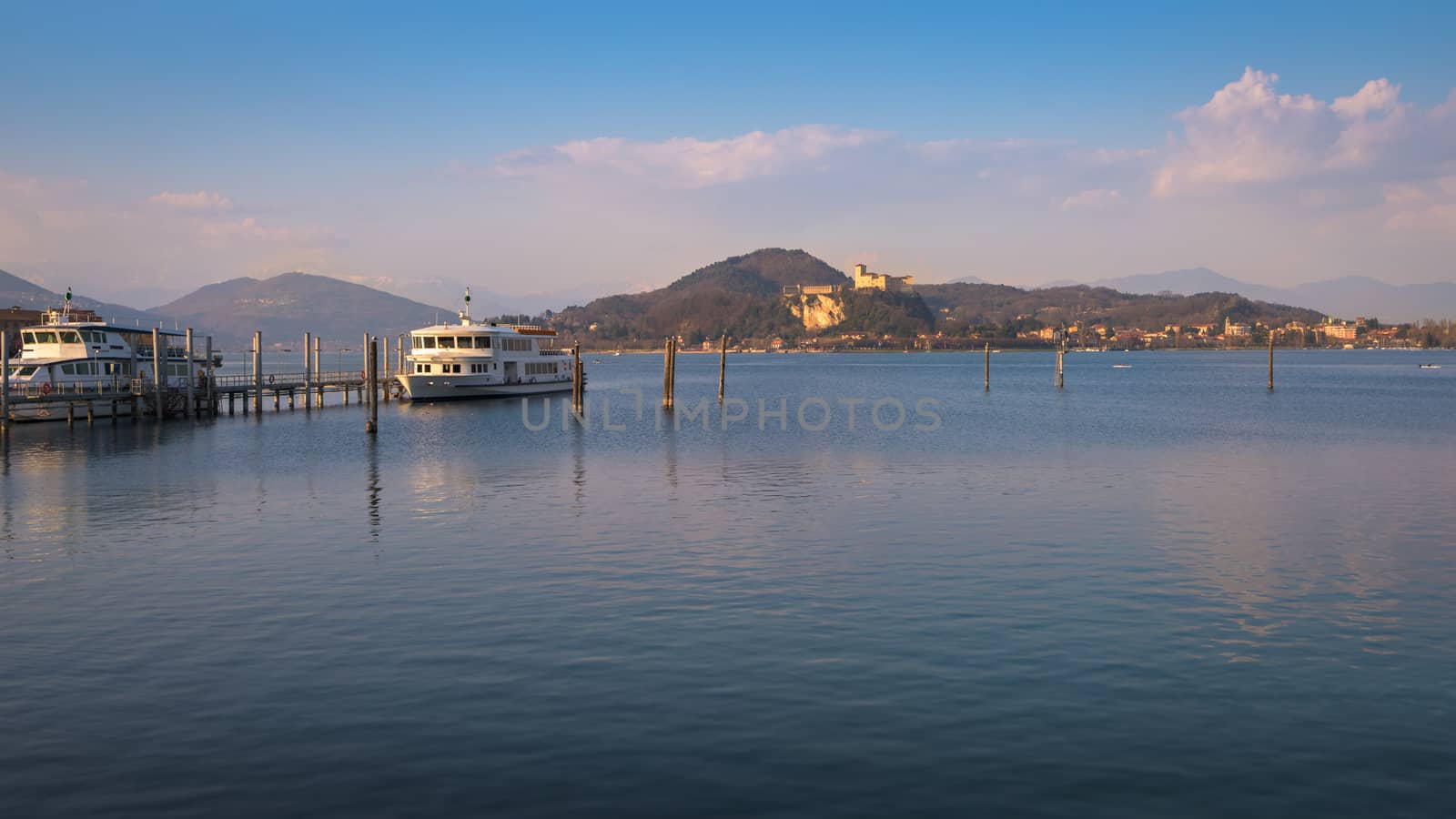 In the picture boats and yachts moored at the port of Arona, Maggiore Lake and in the background the fortress of Angera.