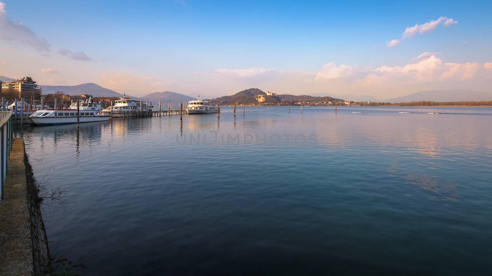 In the picture boats and yachts moored at the port of Arona, Maggiore Lake and in the background the fortress of Angera.