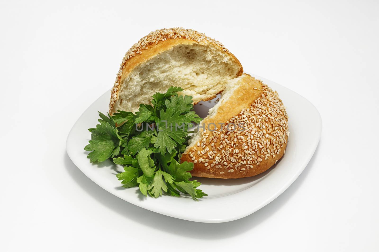 Bun with sesame seeds broken in half on a plate with greens. Shot on a white plastic closeup