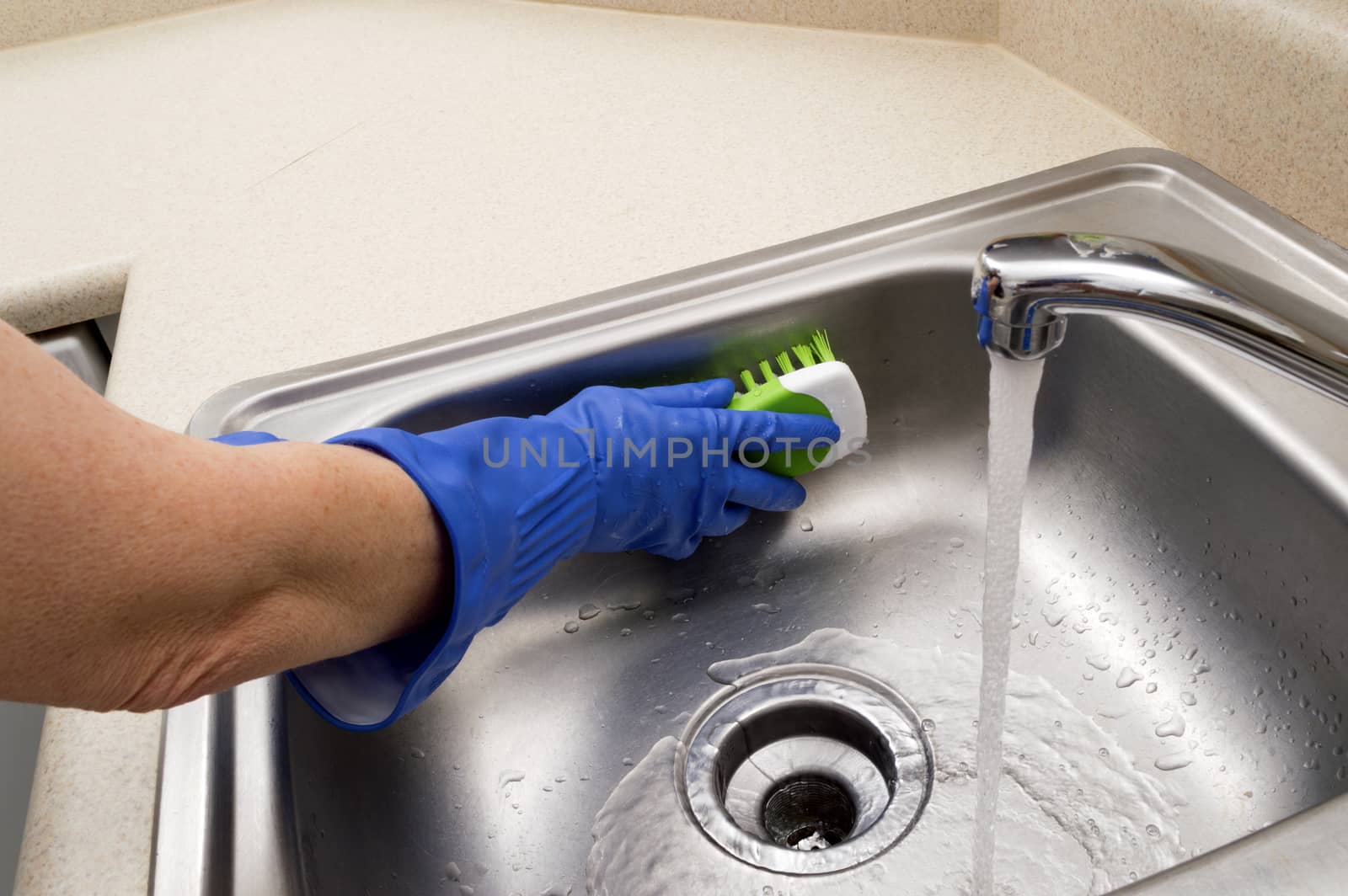 Hands wearing rubber gloves cleaning stainless steel sink.