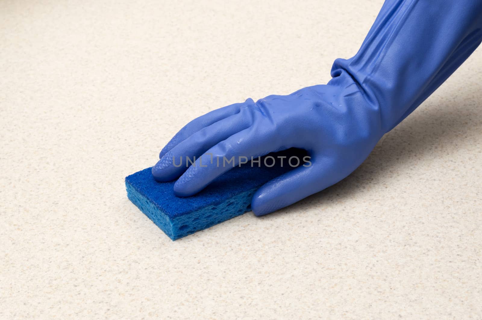 Close up shot of blue gloves and blue sponge cleaning counter top.