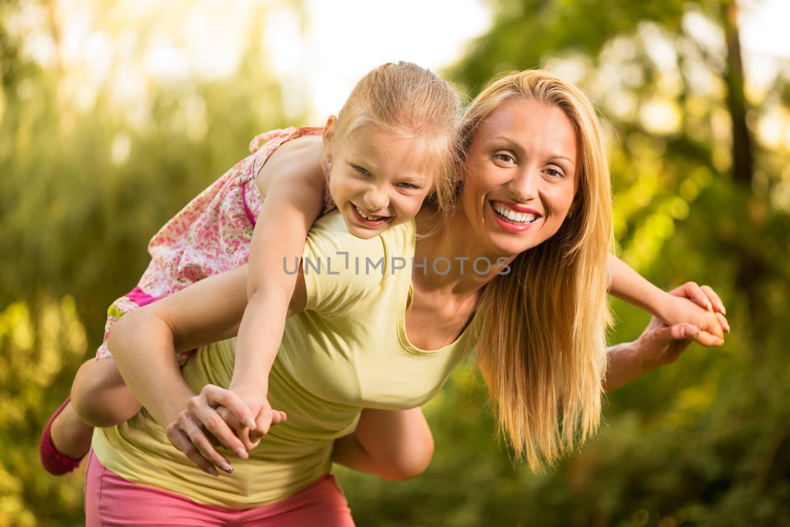 Beautiful mother giving her cute little girl piggyback and smiling in the park