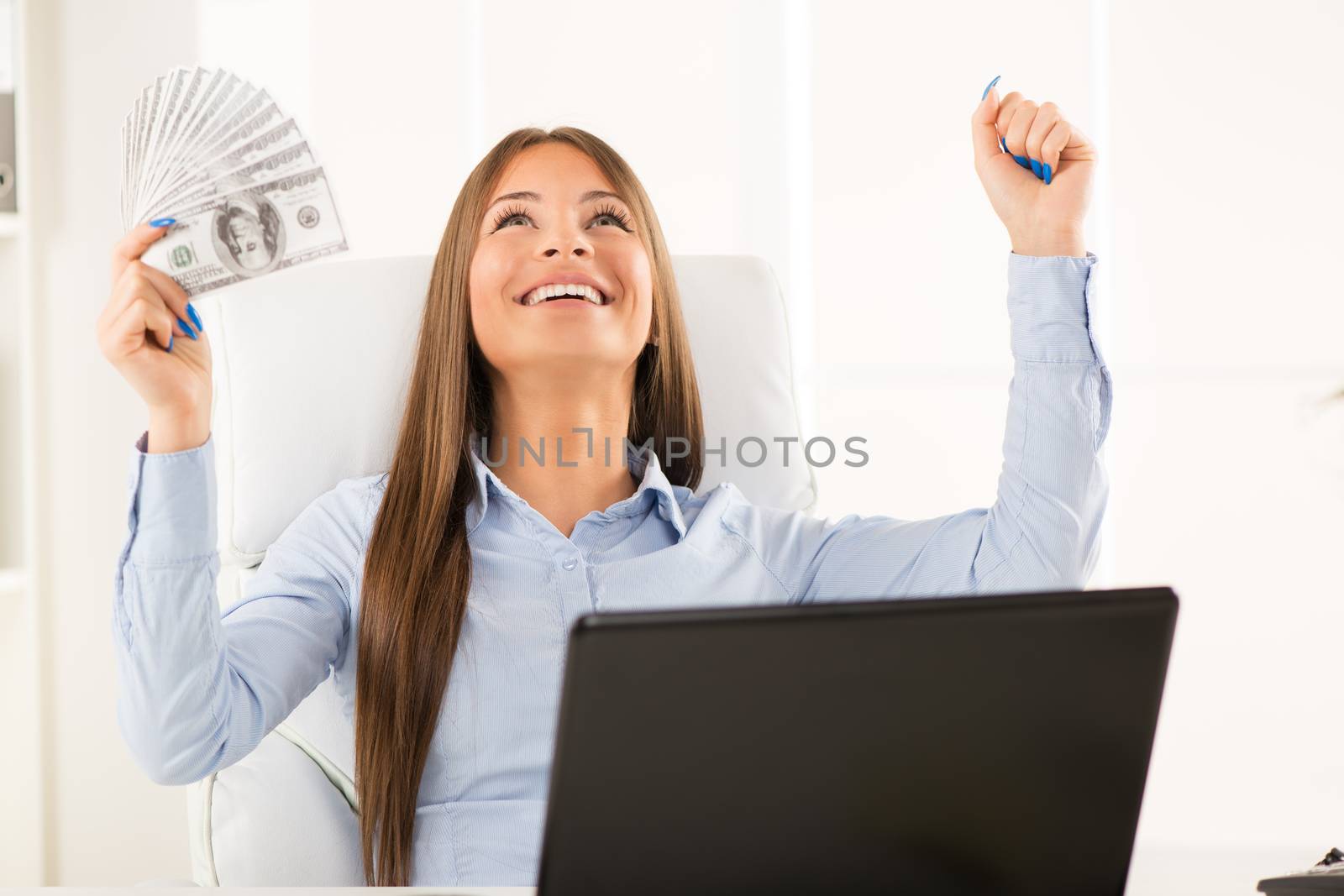 Happy successful Businesswoman in the office holding money with raised arms.