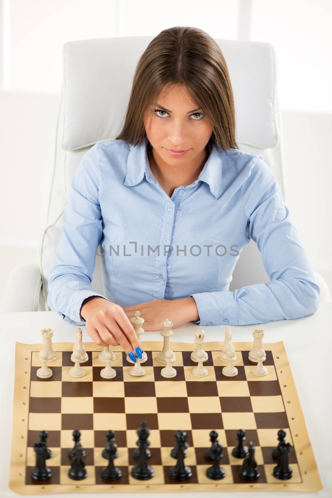 Young beautiful businesswoman devises Business strategy. She sitting above the chessboard with figures and thinking.