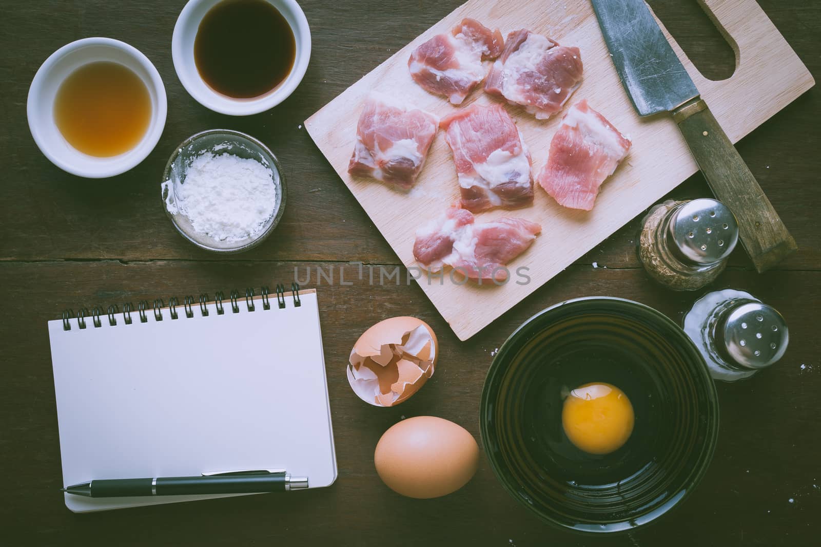 Preparation for cooking in home kitchen. Soft pork ribs on chopping board, notepad for check list, egg, and ingredients on wood table with vintage filter effect