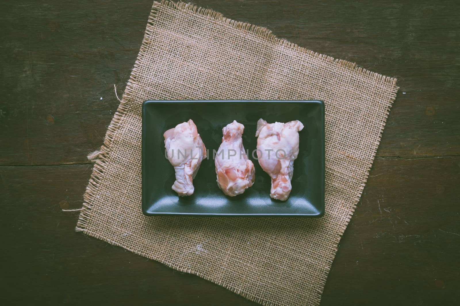 Preparation for cooking in home kitchen. Chicken wings in ceramic dish on wood table with vintage filter effect