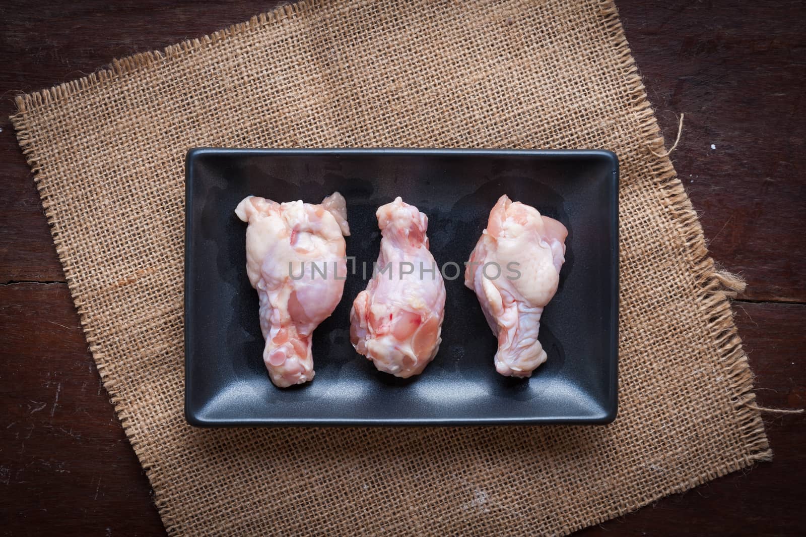 Preparation for cooking in home kitchen. Chicken wings in ceramic dish on wood table.