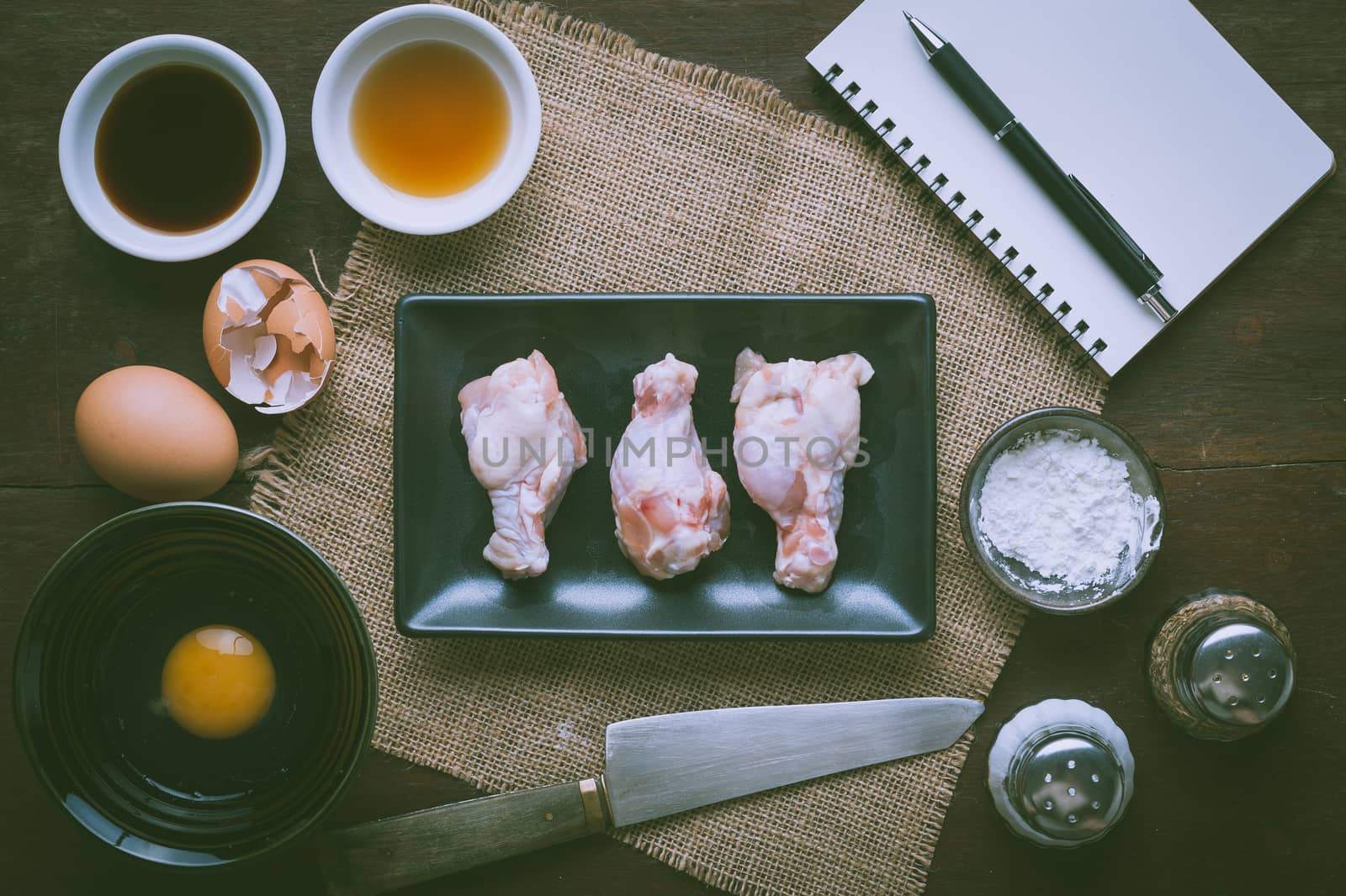 Preparation for cooking in home kitchen. Chicken wings in ceramic dish and ingredients on wood table with vintage filter effect.