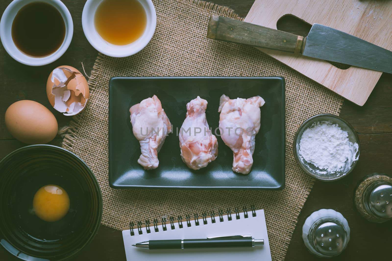 Preparation for cooking in home kitchen. Chicken wings in ceramic dish and ingredients on wood table with vintage filter effect.