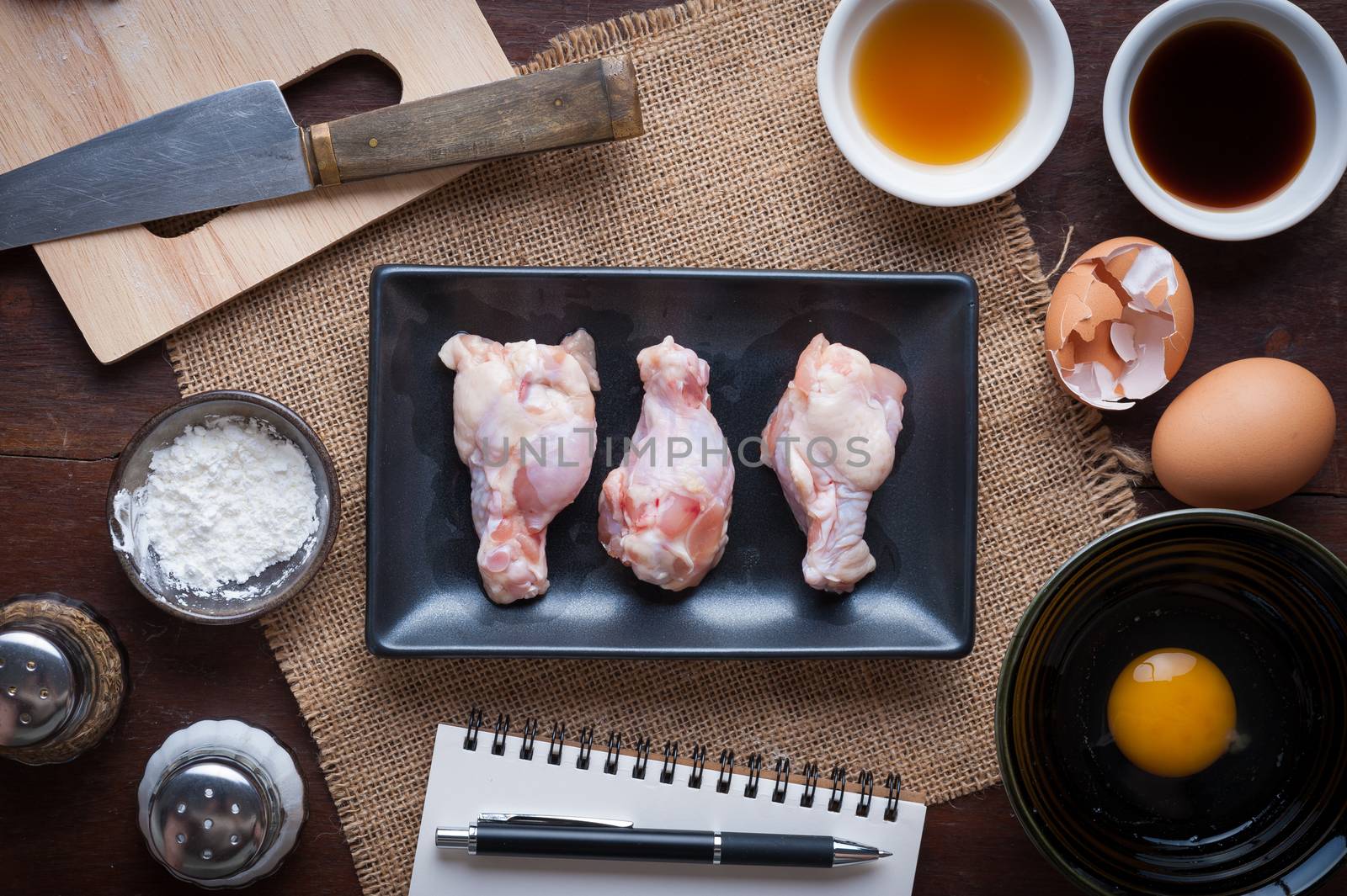Preparation for cooking in home kitchen. Chicken wings in ceramic dish and ingredients on wood table.