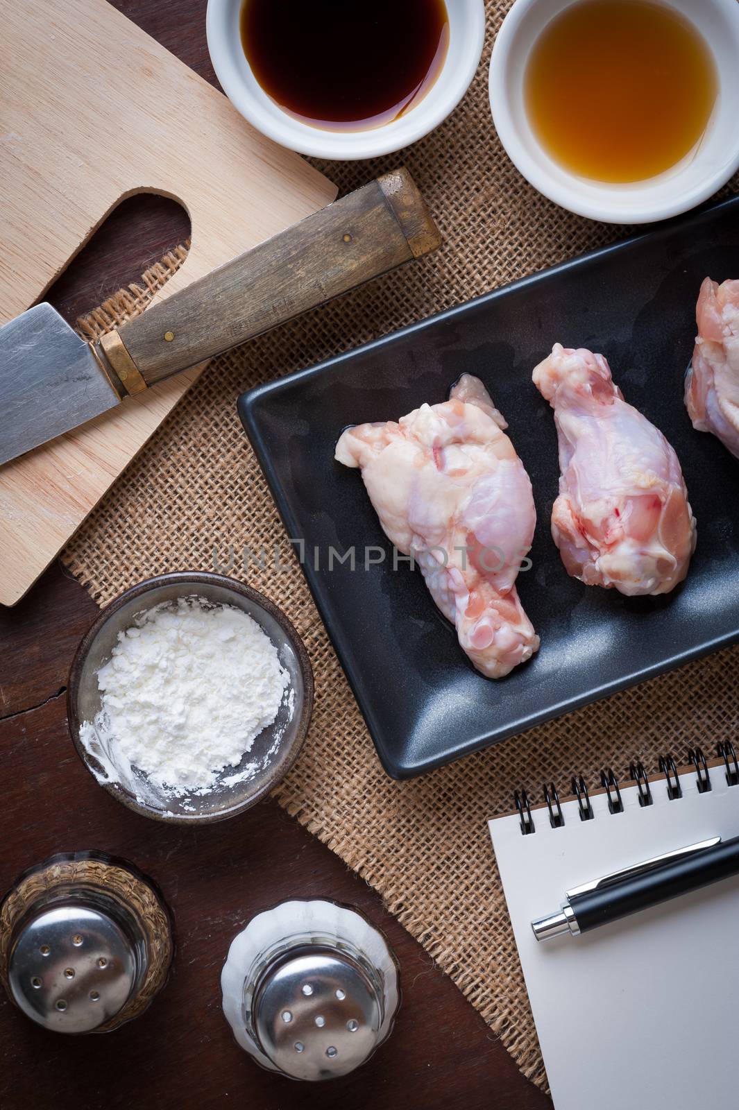 Preparation for cooking in home kitchen. Chicken wings in ceramic dish and ingredients on wood table.
