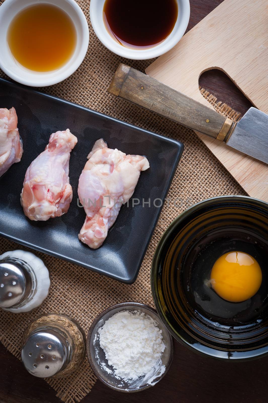 Preparation for cooking in home kitchen. chicken wings in ceramic dish, eggs, and ingredients on wood table.