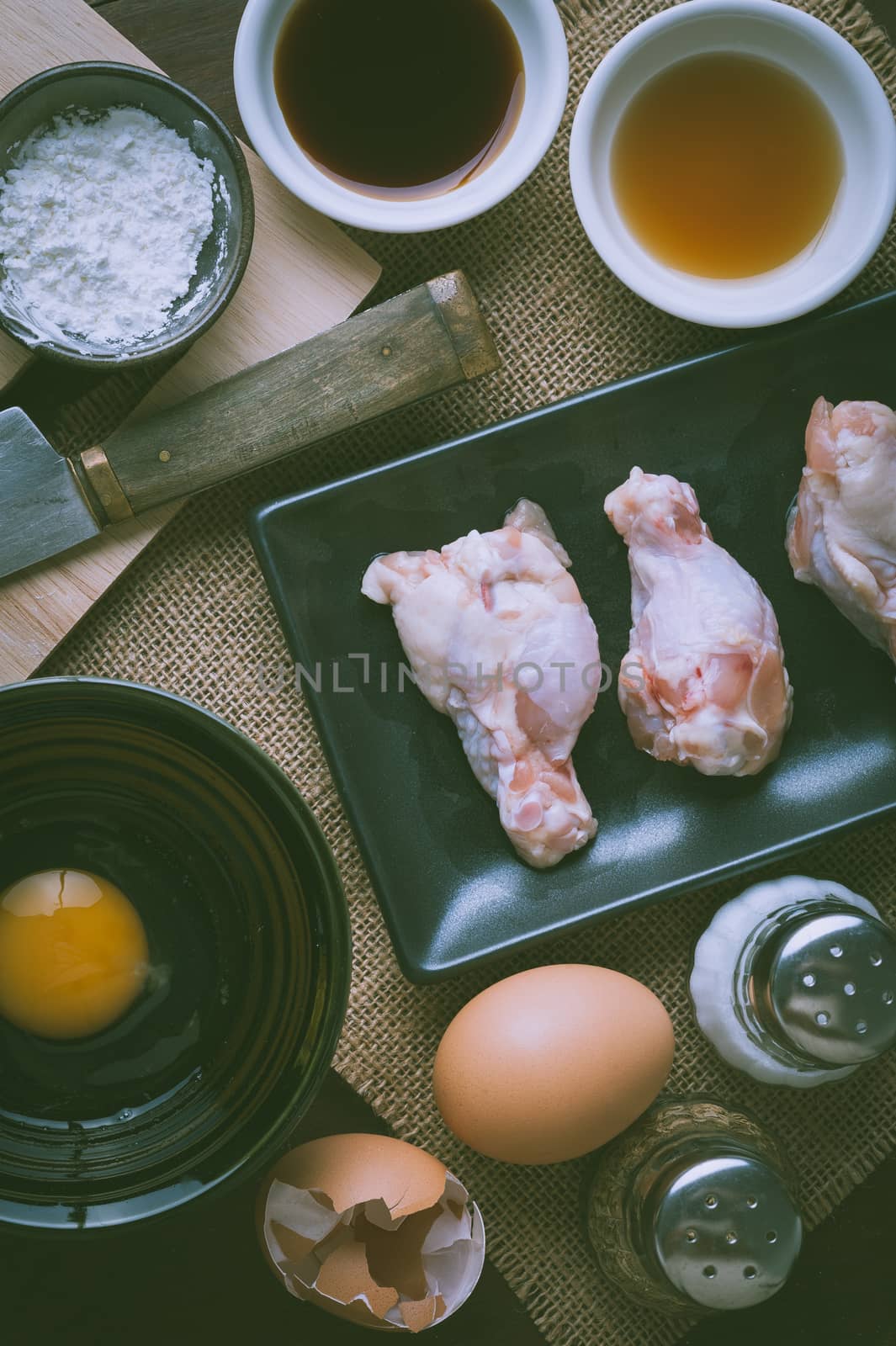 Preparation for cooking in home kitchen. chicken wings in ceramic dish, eggs, and ingredients on wood table with vintage filter effect.