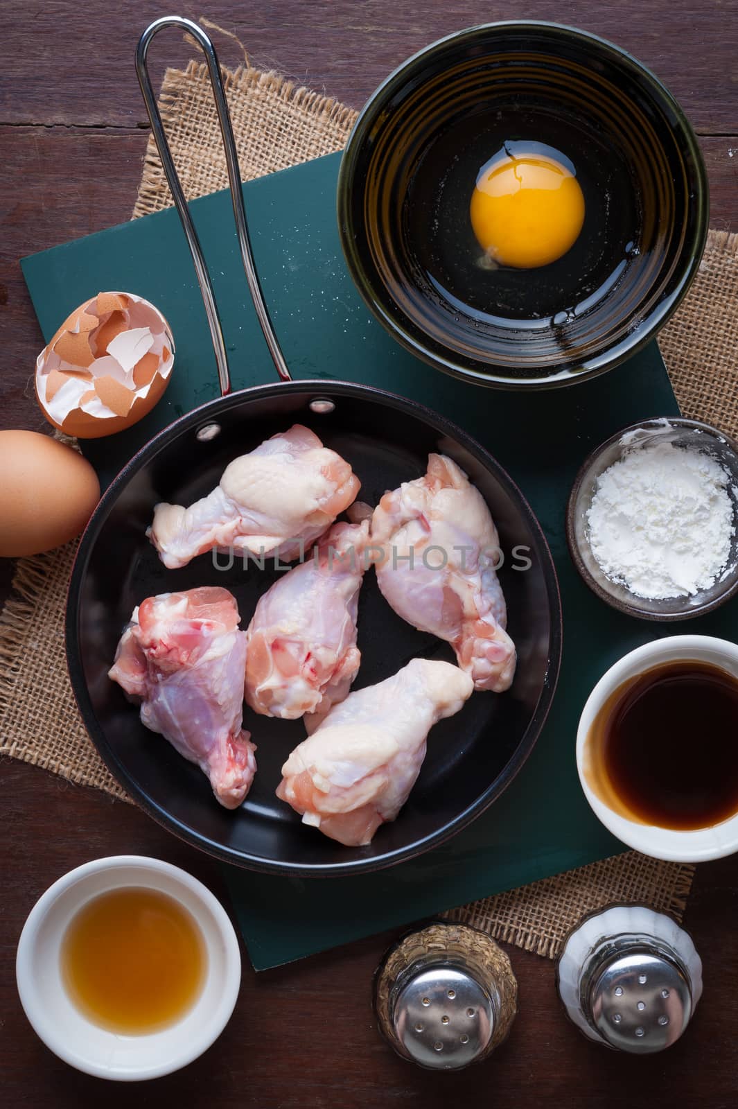 Preparation for cooking in home kitchen. chicken wings in small pan, eggs, and ingredients on wood table.