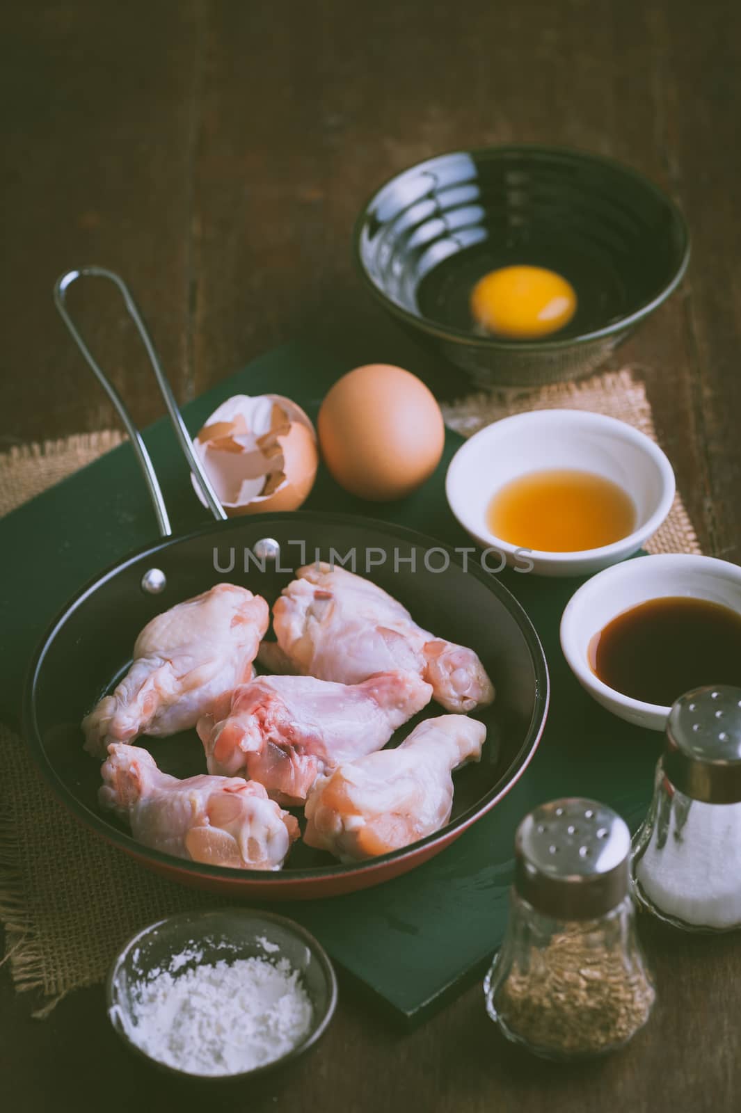 Preparation for cooking in home kitchen. chicken wings in small pan, eggs, and ingredients on wood table with vintage filter effect