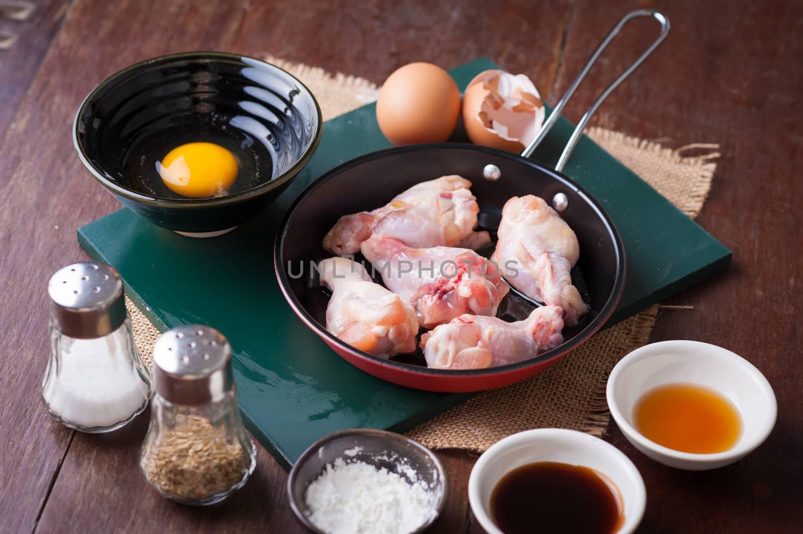 Preparation for cooking in home kitchen. chicken wings in small pan, eggs, and ingredients on wood table.