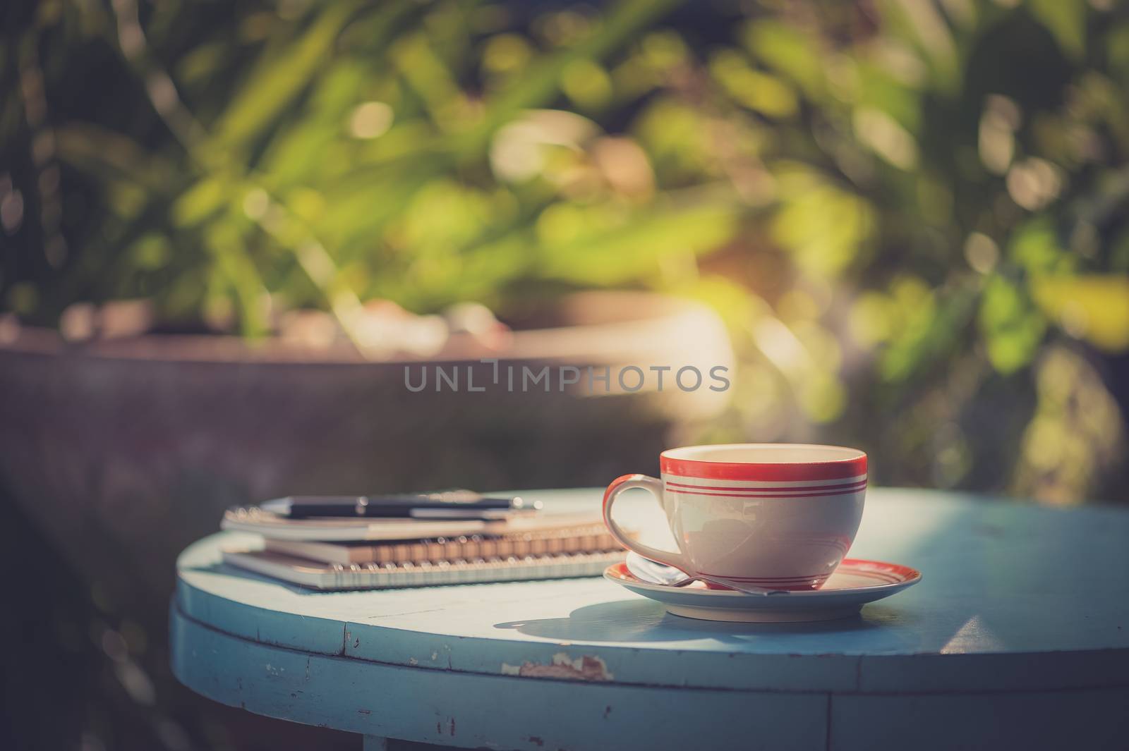 Coffee cup, notebooks, and pen on blue veteran table in morning time with vintage filter effect
