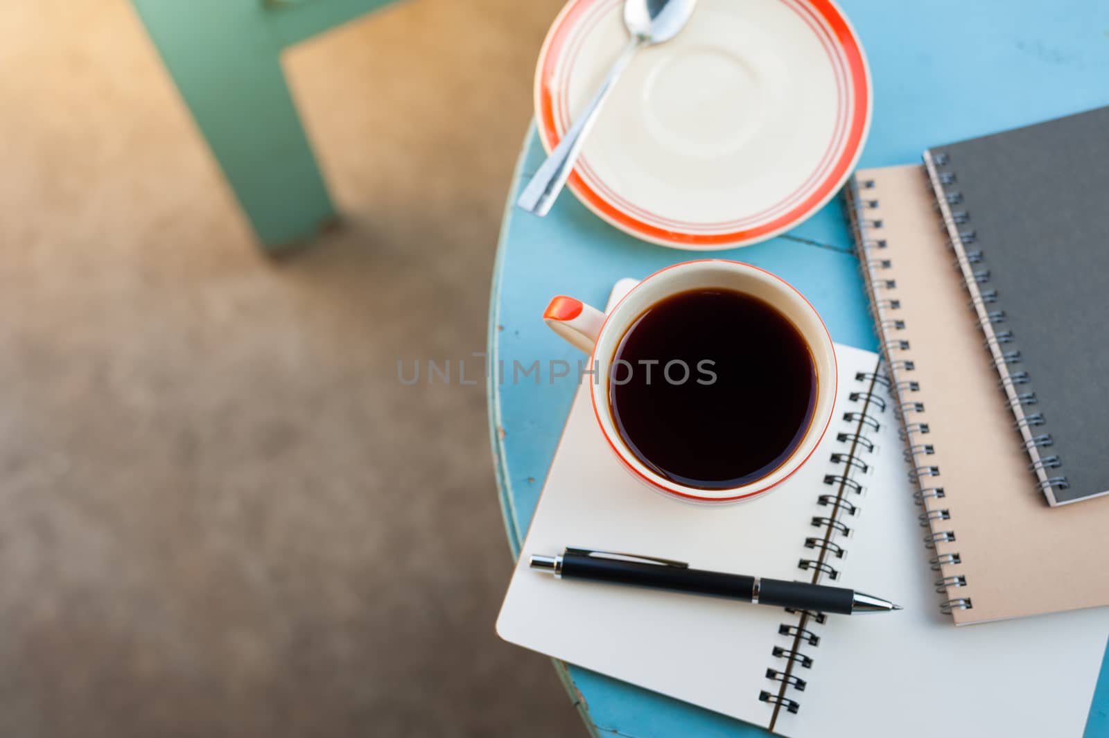 Coffee cup with notebooks and pen on blue round wood table in morning time