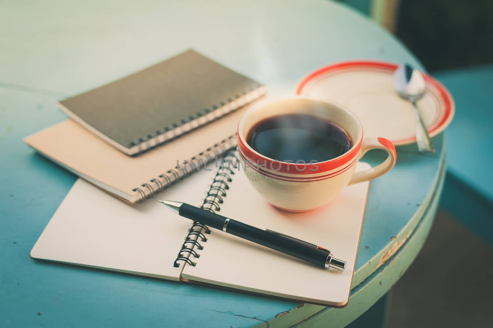 Coffee cup with notebooks and pen on blue round wood table in morning time with vintage filter effect