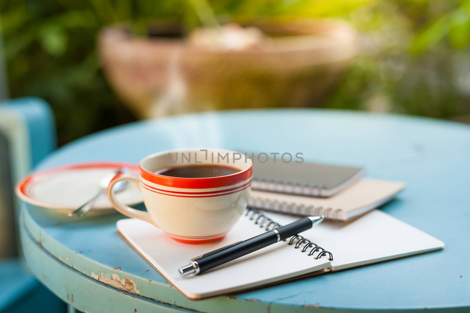 Coffee cup with notebooks and pen on blue round wood table in morning time