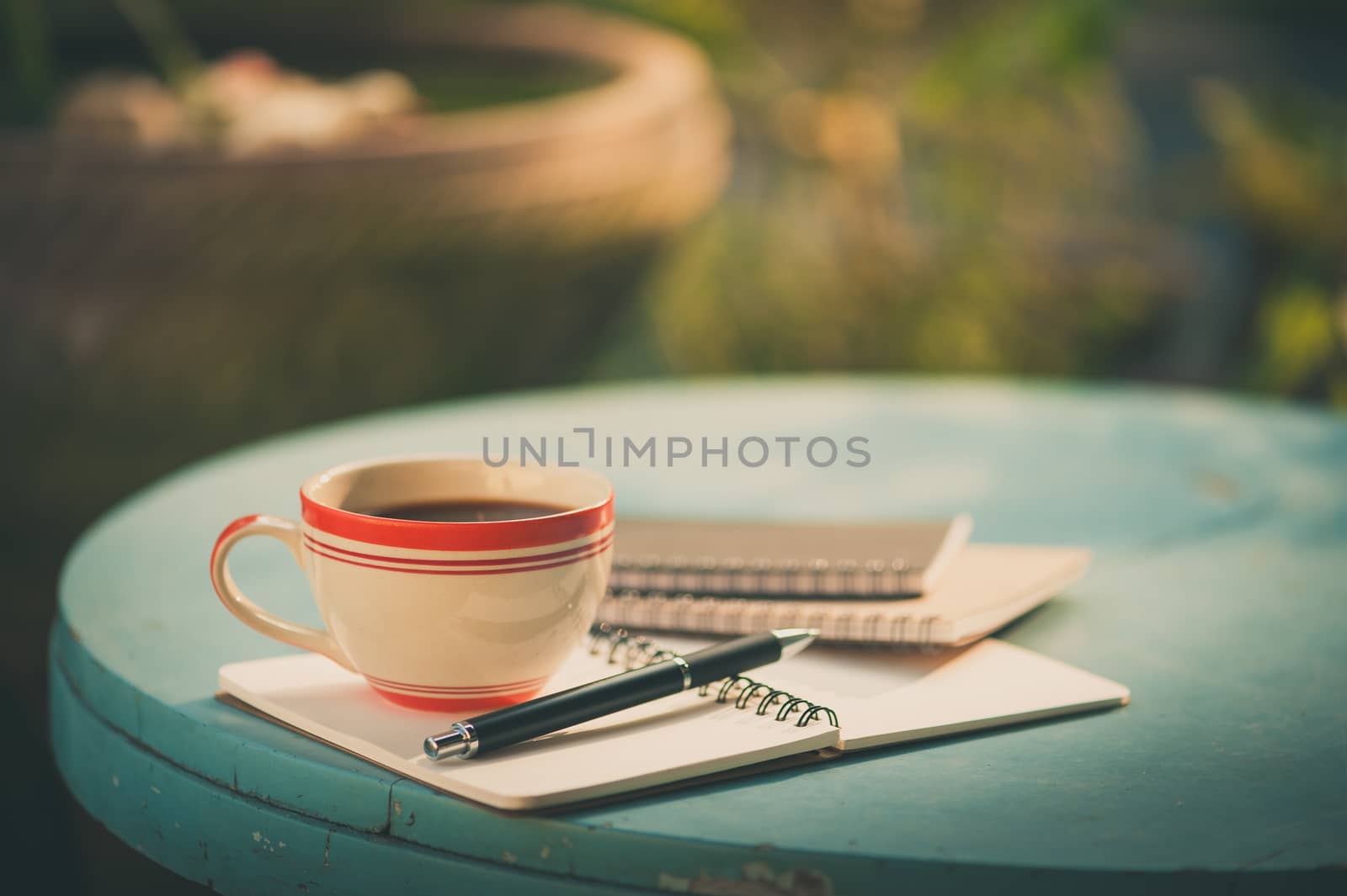 Coffee cup with notebooks and pen on blue round wood table in morning time with film filter effect
