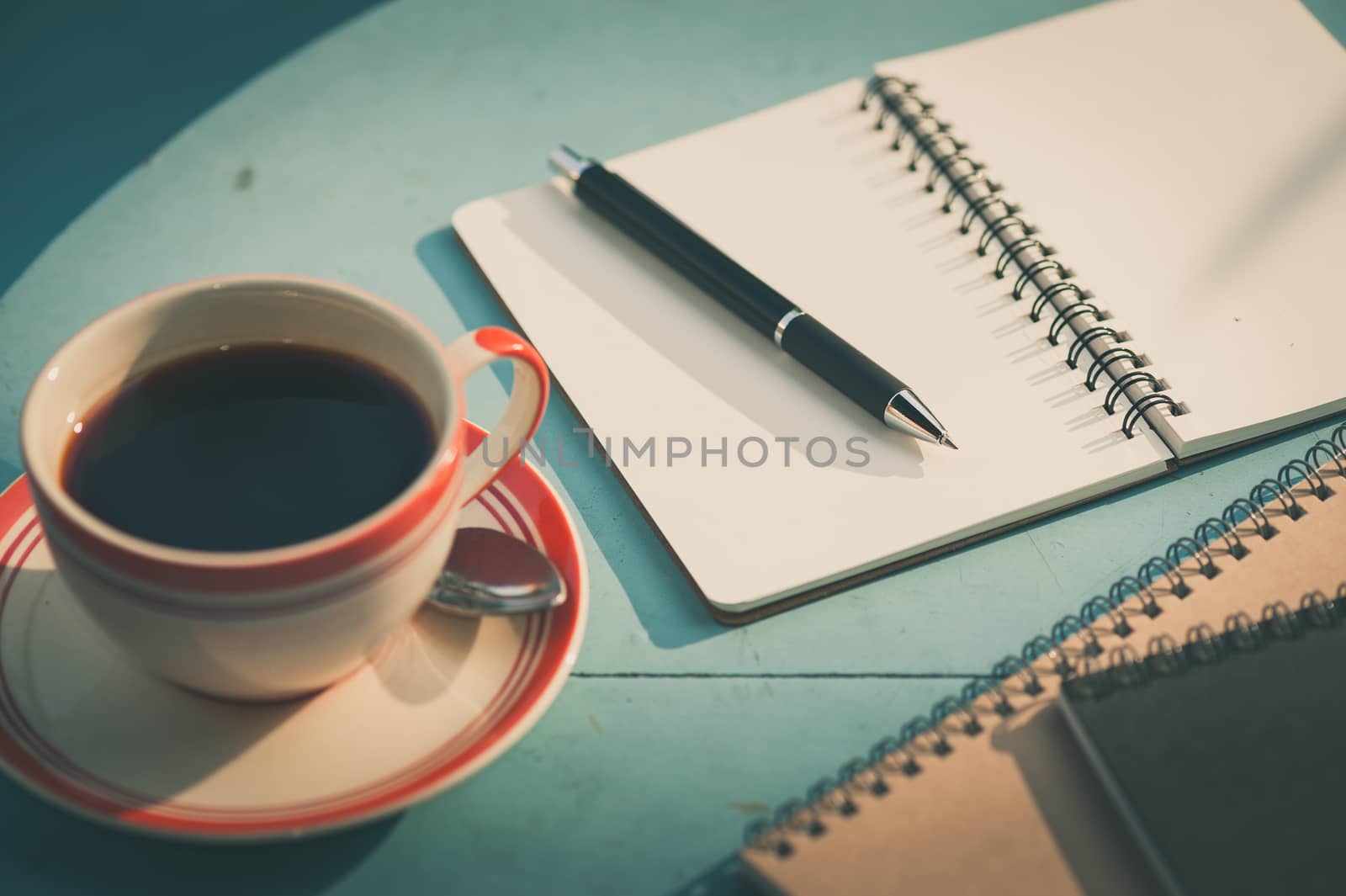 Small notebook and pen beside coffee cup on blue wood table at outdoor area in cafe with morning scene and vintage filter effect