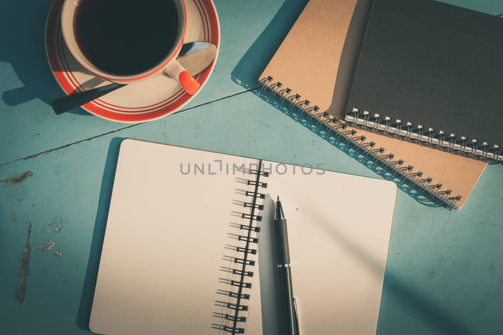 Morning scene of small notebook and pen beside coffee cup on blue wood table at outdoor area in cafe with vintage filter effect