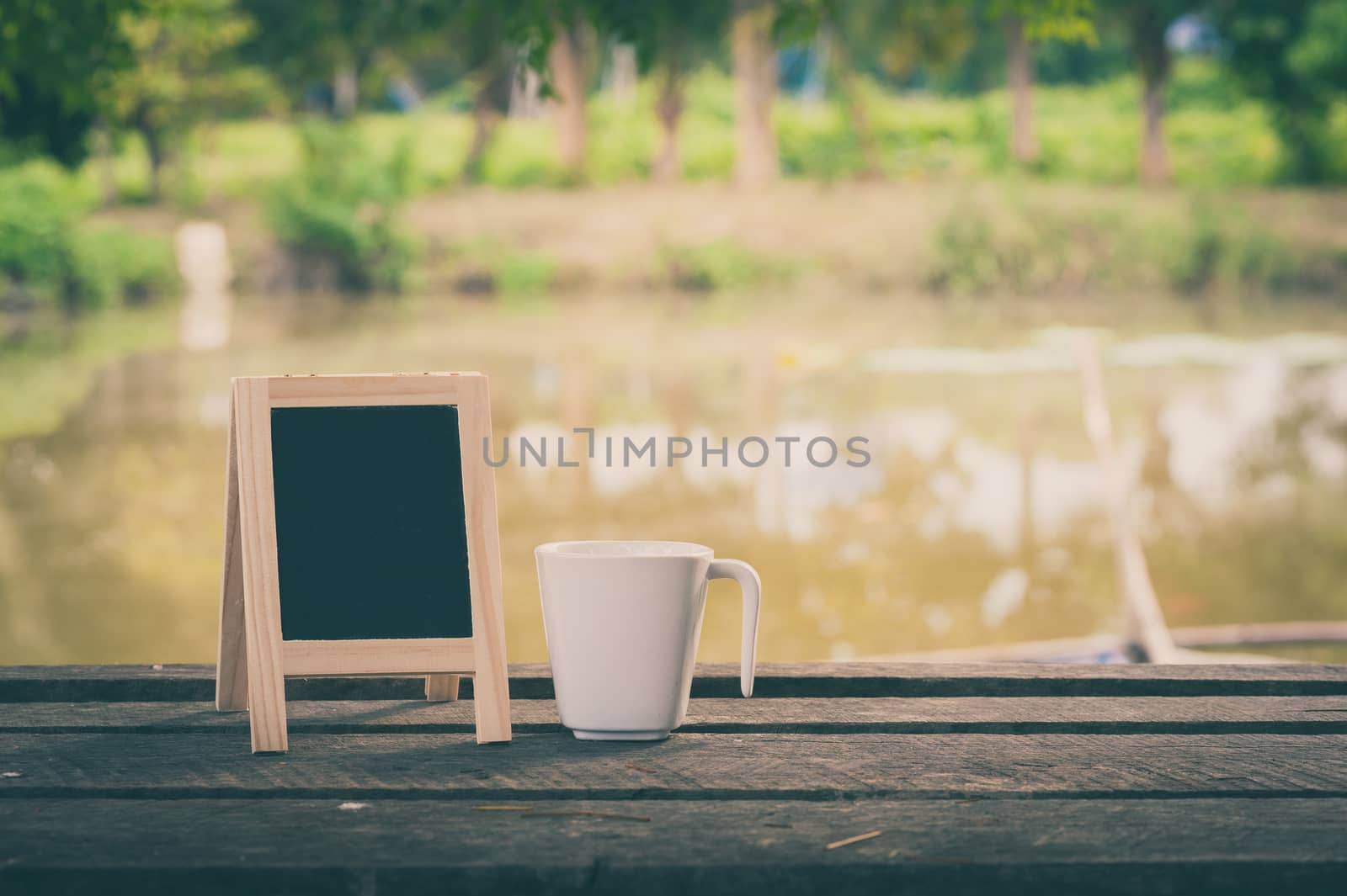 Small A-frame blackboard with blank area for text or message and coffee cup on rustic wood table in morning time with vintage filter effect