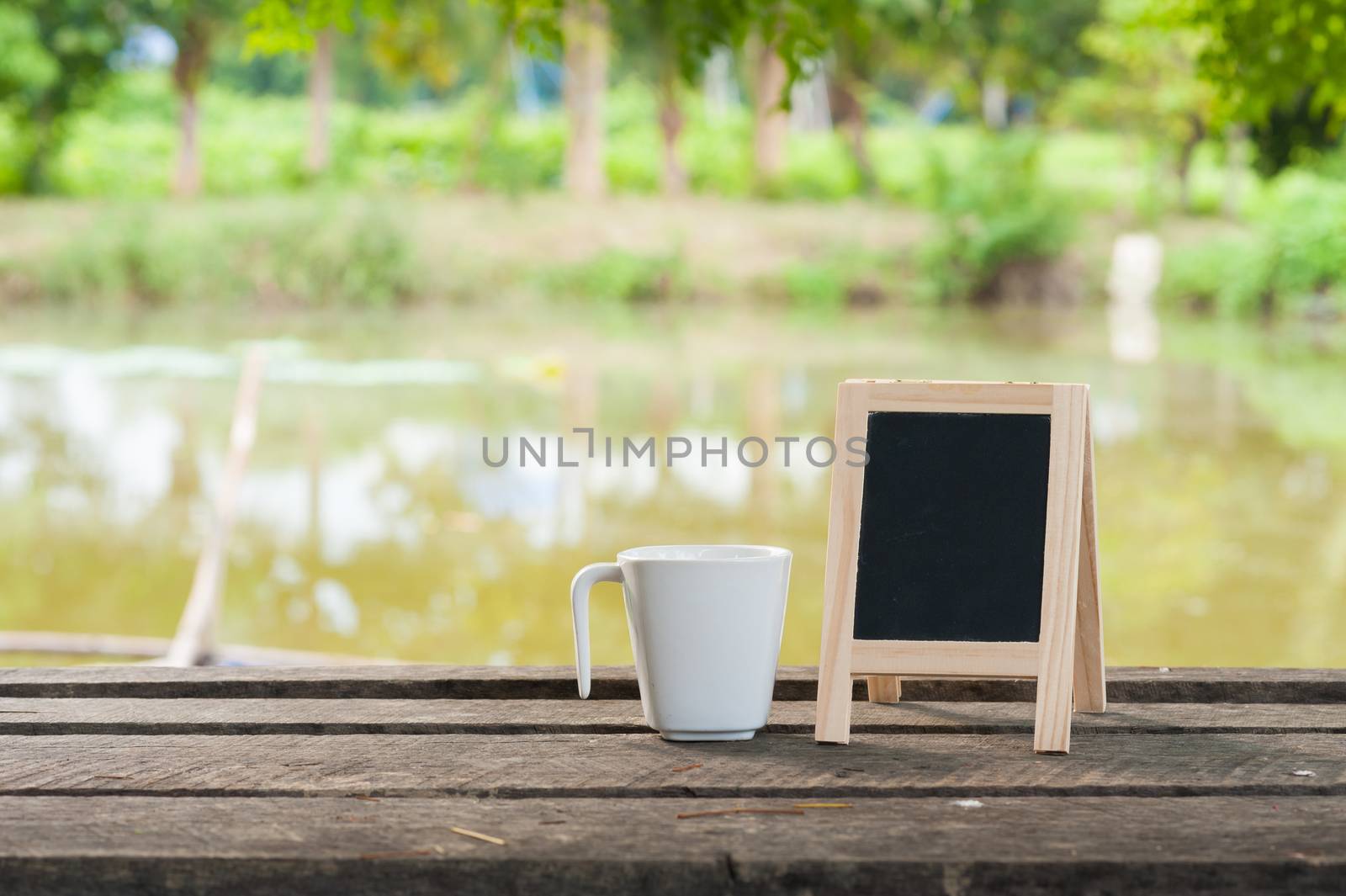 Small A-frame blackboard with blank area for text or message and coffee cup on rustic wood table in morning time